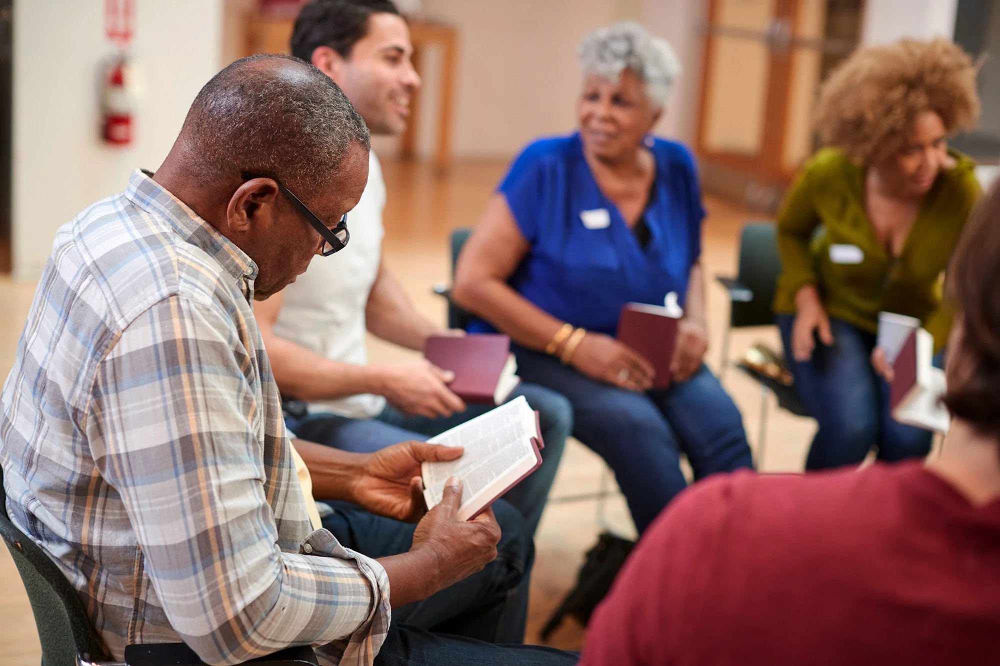 A group of diverse people sitting in a circle, reading books, engaged in a discussion in a community room.