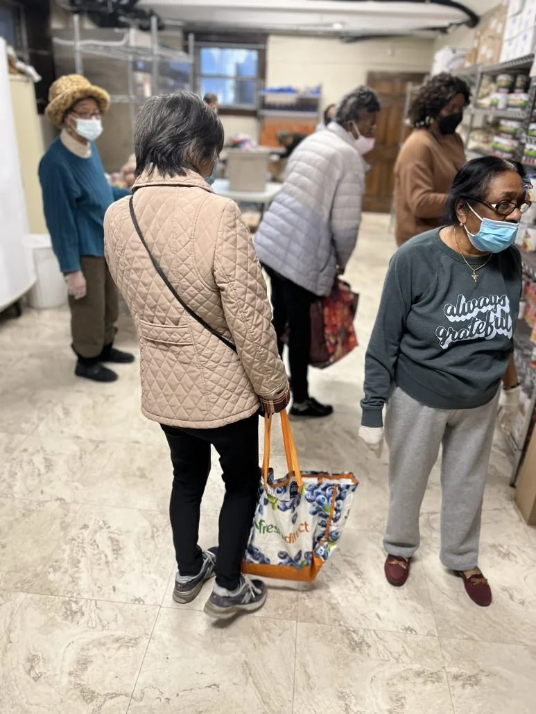 A group of women, wearing face masks, line up inside a store, possibly shopping for groceries or products on shelves.
