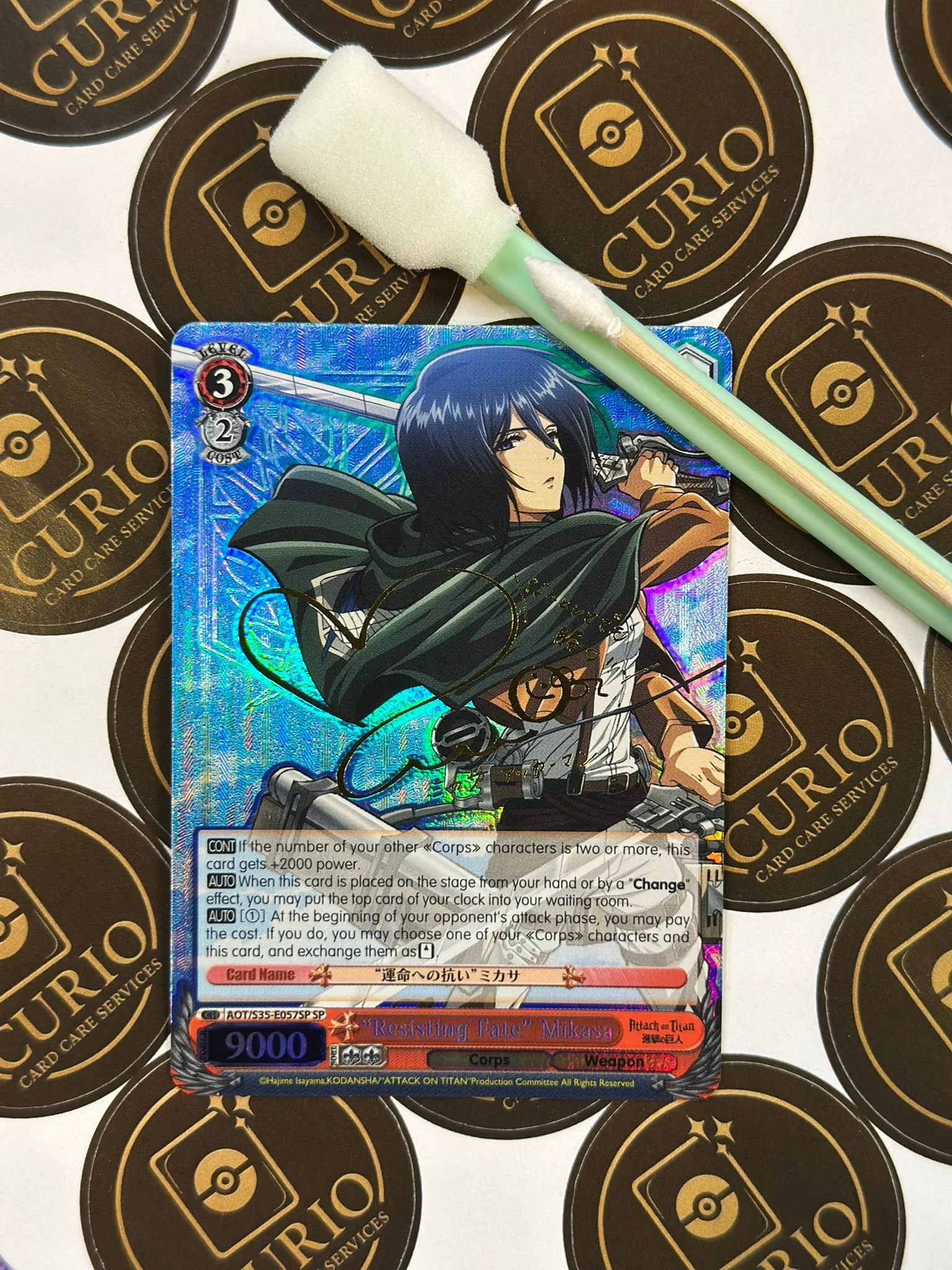 Hands wearing gray gloves handling a Pokémon trading card with a drawing of a yellow and blue dragon, a purple liquid in a measuring beaker, and a large container of mirror coat spray on a purple surface.