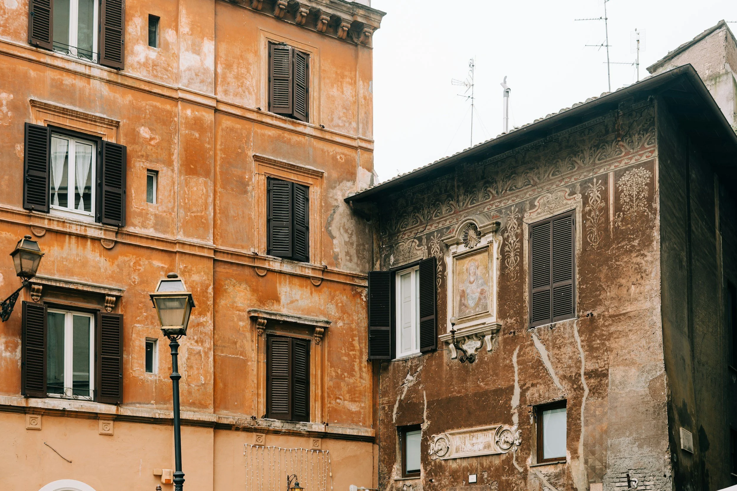 Edificio storico con pareti di colore arancione e decorazioni, finestre con persiane nere, lampione in primo piano.