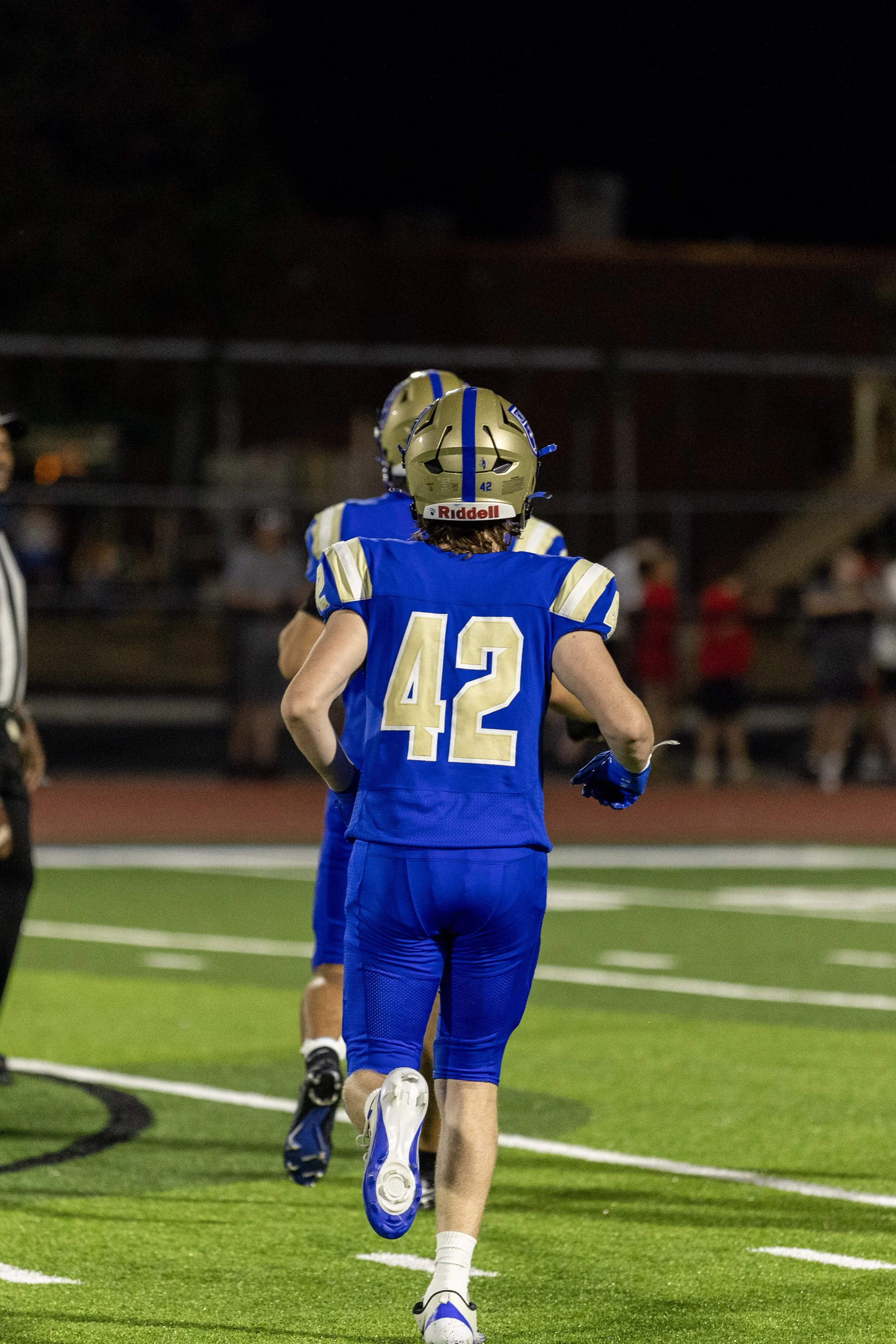A football player wearing a blue and gold uniform with number 42 on the back, running on a football field at night.