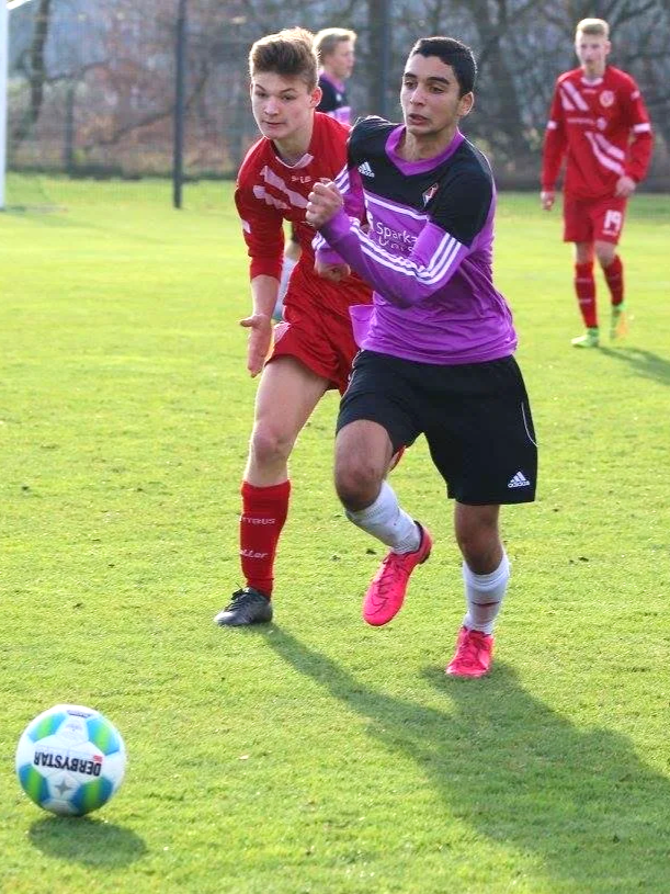 Two soccer players competing for the ball on the field during a match, with two additional players in the background.