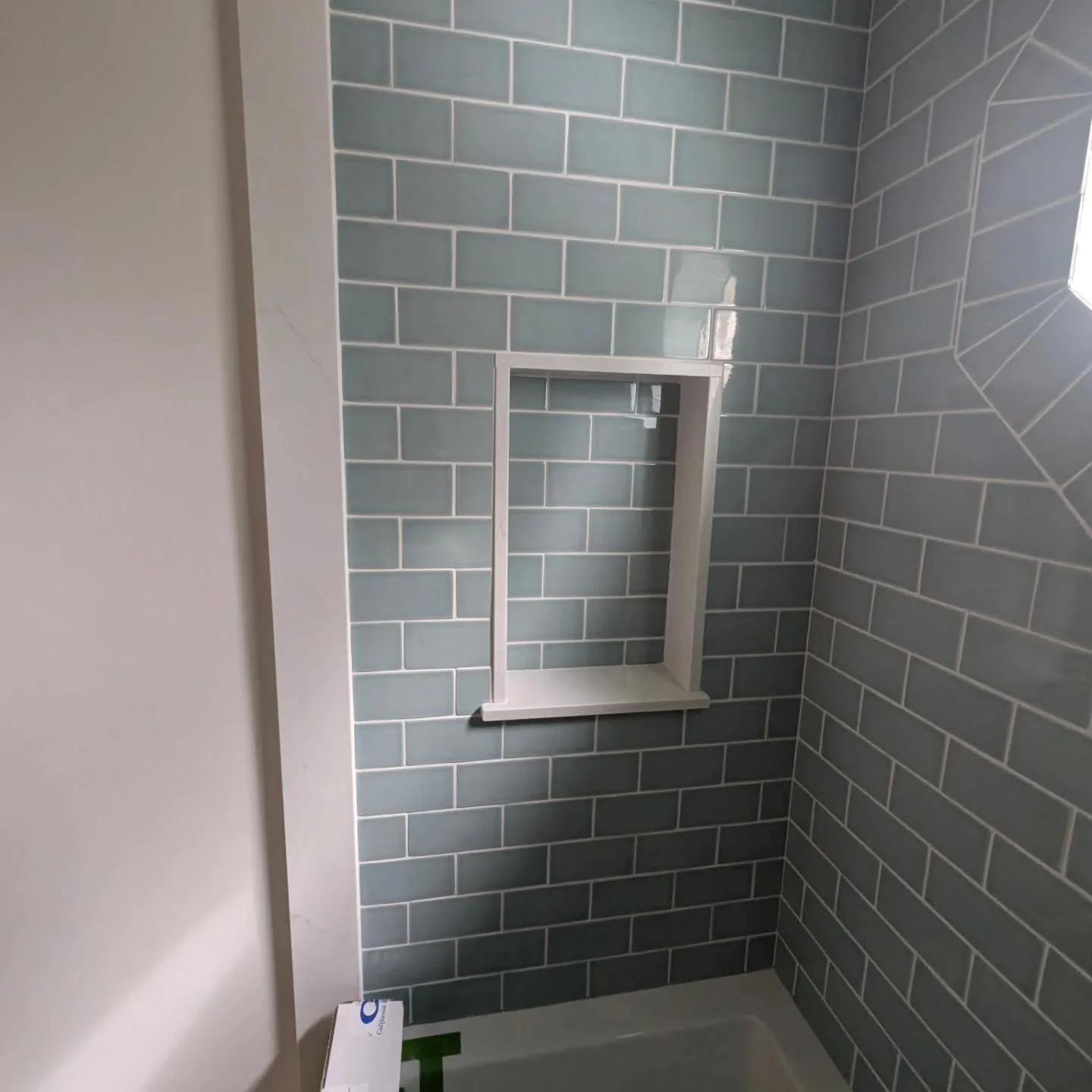 Niche and wainscott cased with white ceasar stone. Blue handmade subway tile by @annsacks. Cool window!