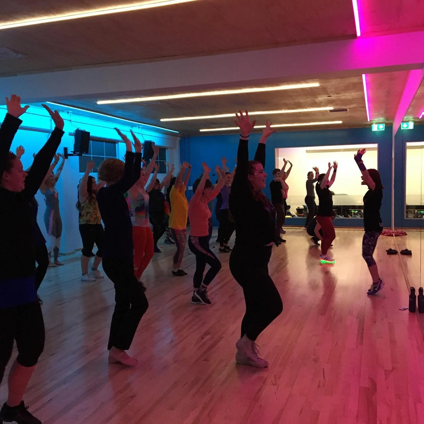 A group of adults dancing with their arms up while a teacher demonstrates at the front of the class