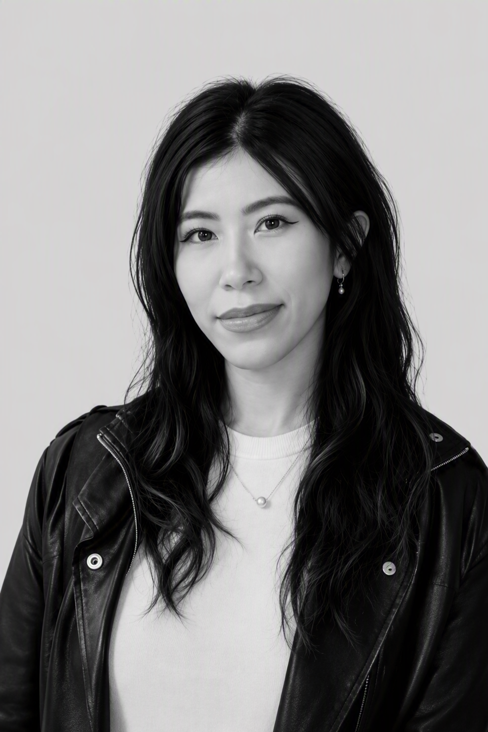 Black and white portrait of a woman smiling, wearing a collared shirt, earrings, and a necklace, sitting against a plain background.