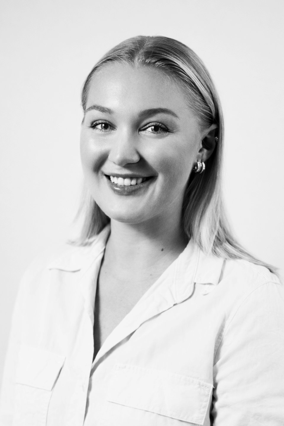 Black and white portrait of a woman with long wavy hair, wearing a white top and smiling.