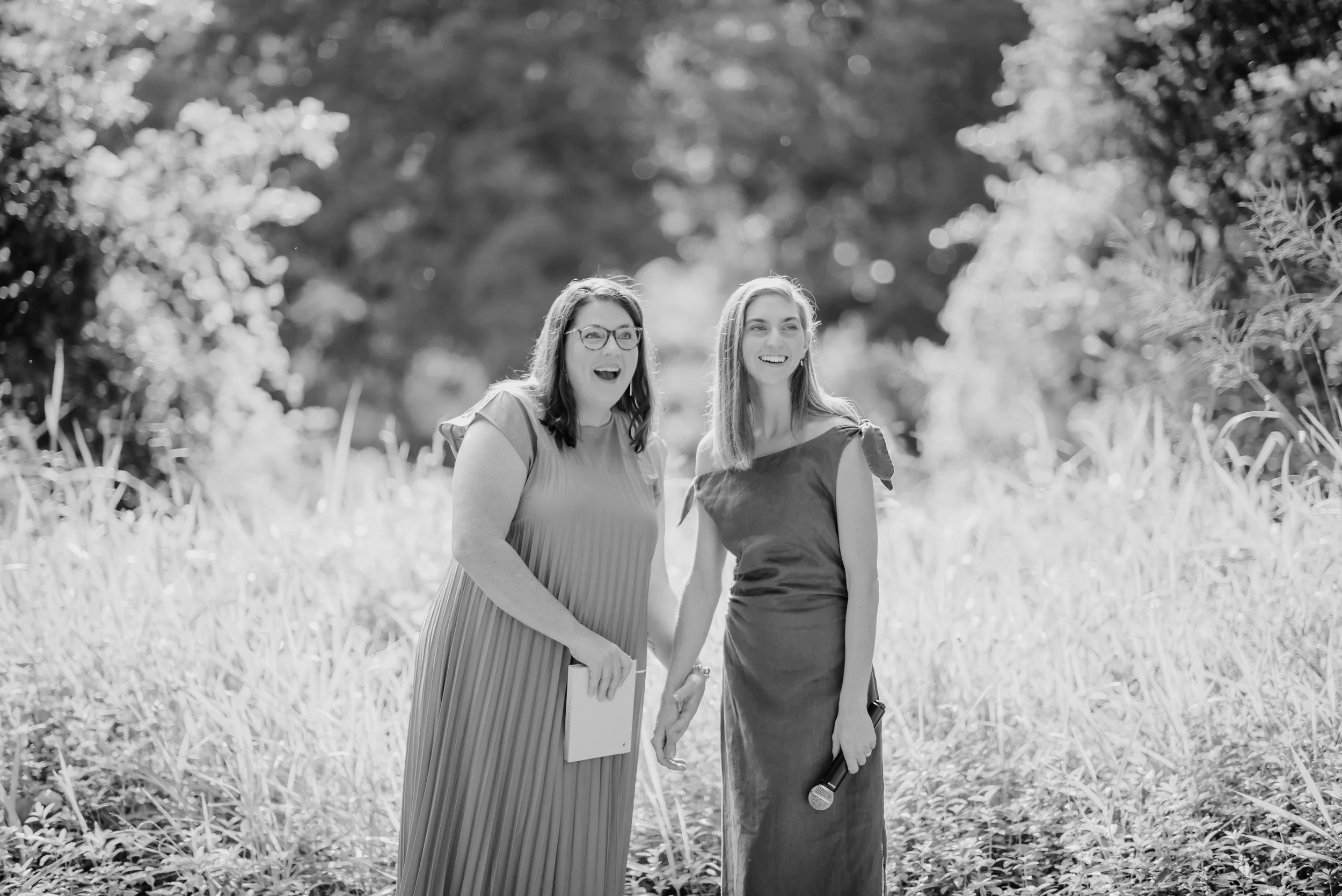 Two marriage celebrants, Brisbane-based, smiling as they deliver a wedding ceremony, one holding a microphone.