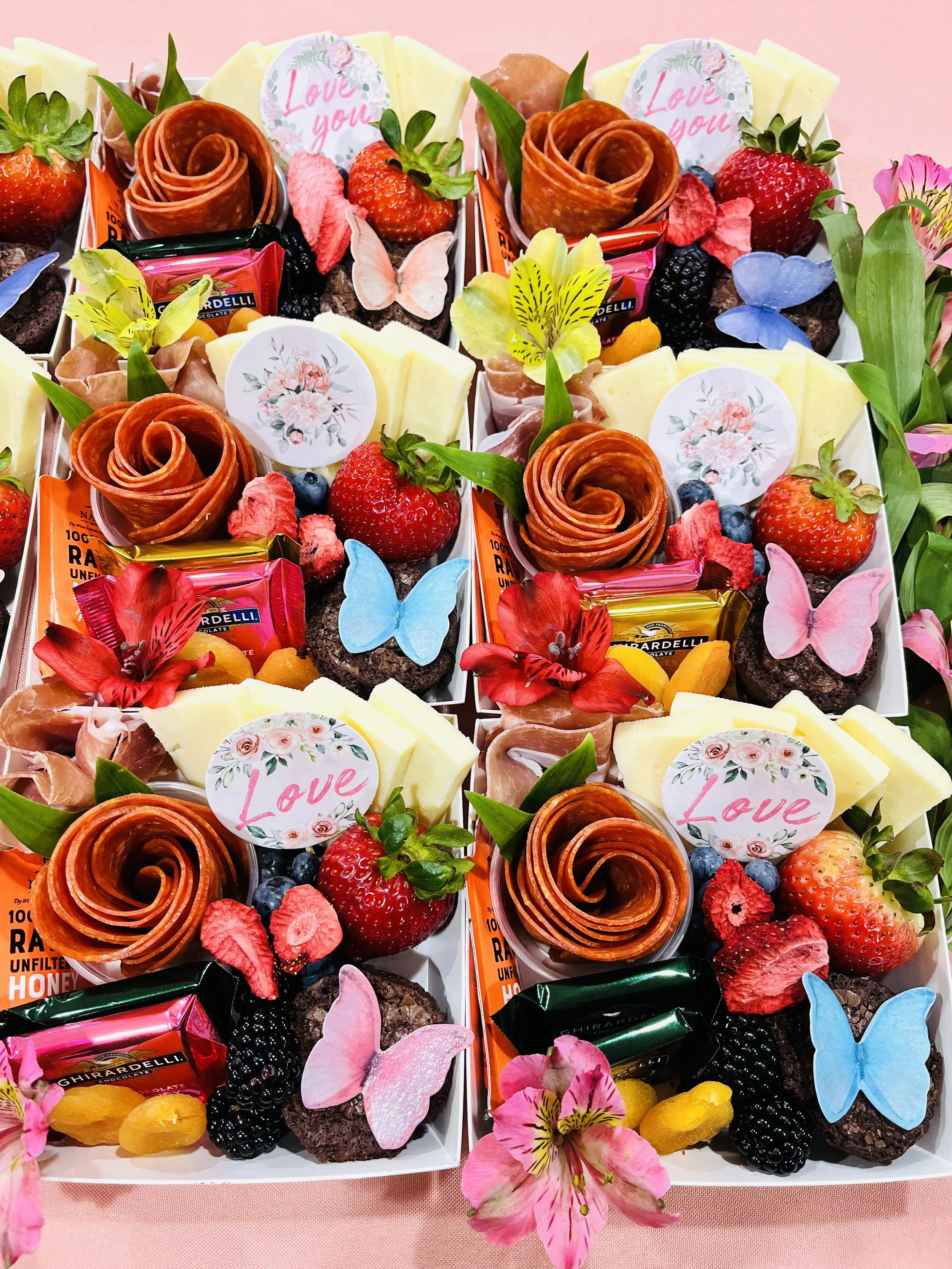 Colorful gift boxes filled with strawberries, blackberries, blueberries, cheese, chocolates, cookies, flowers, and decorative butterflies and 'Love you' tags.