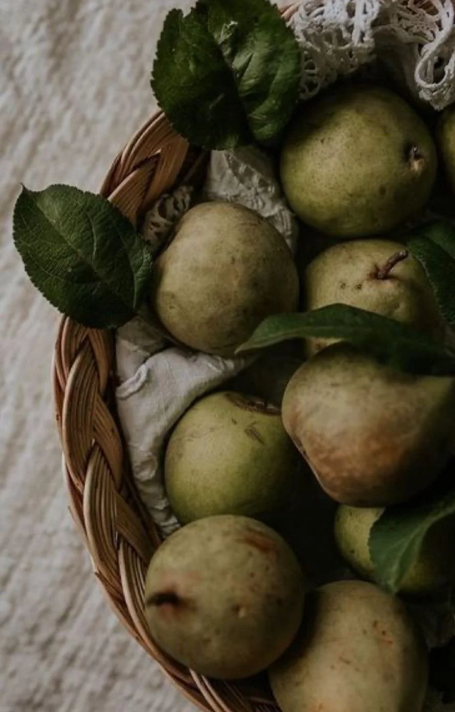 A basket of fresh green pears with leaves on a rustic wooden surface.