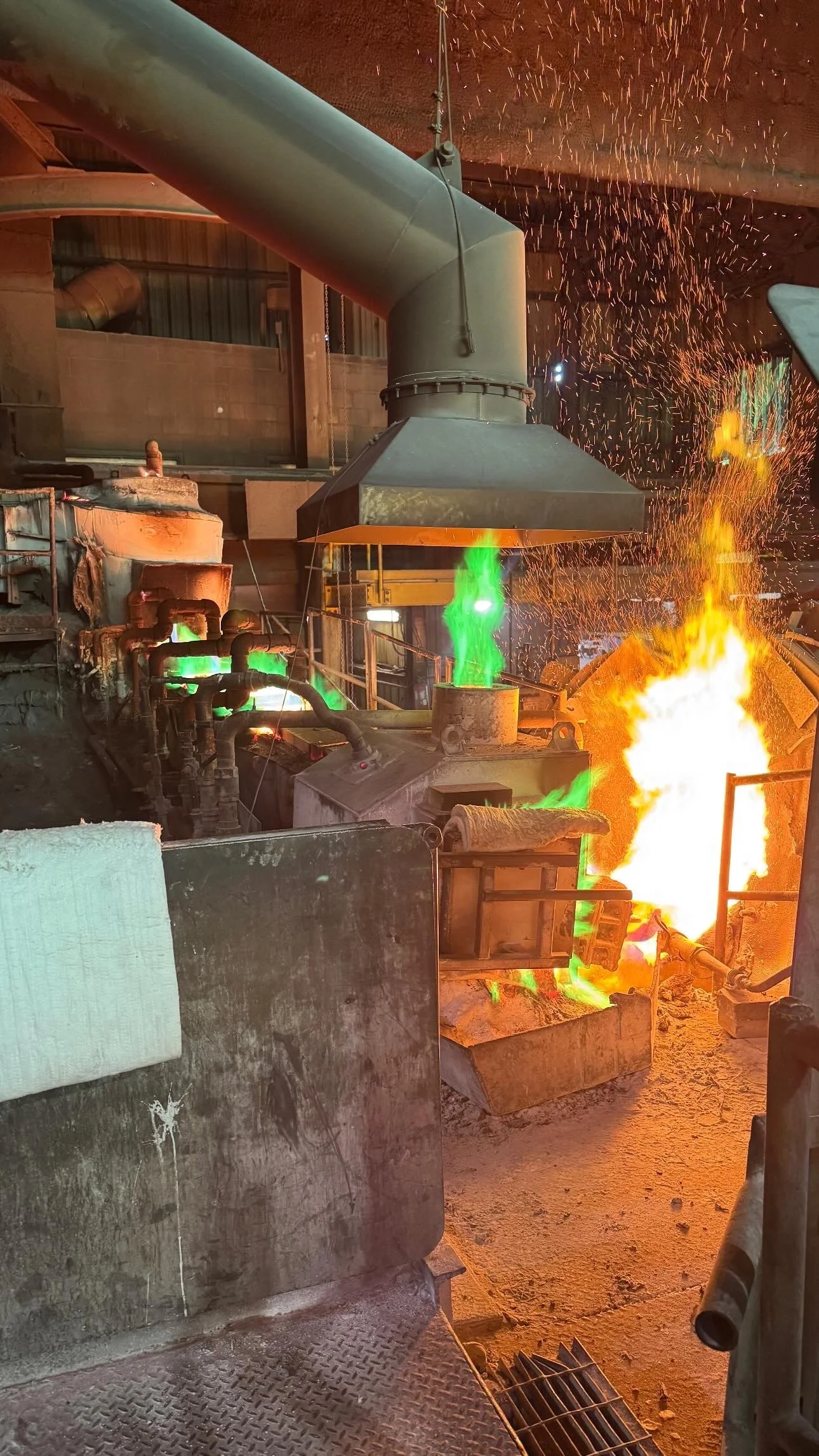 A blacksmith forge with sparks flying, glowing green and orange hot metal, and flames in an industrial workshop.
