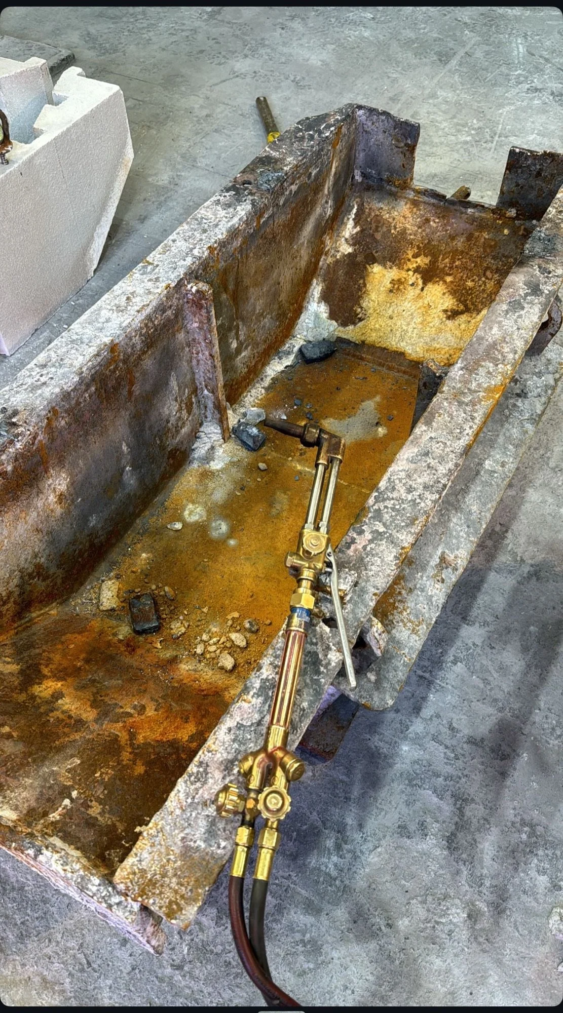 A rusty, old metal container with some water and debris inside, and a brass welding or cutting torch resting on it.