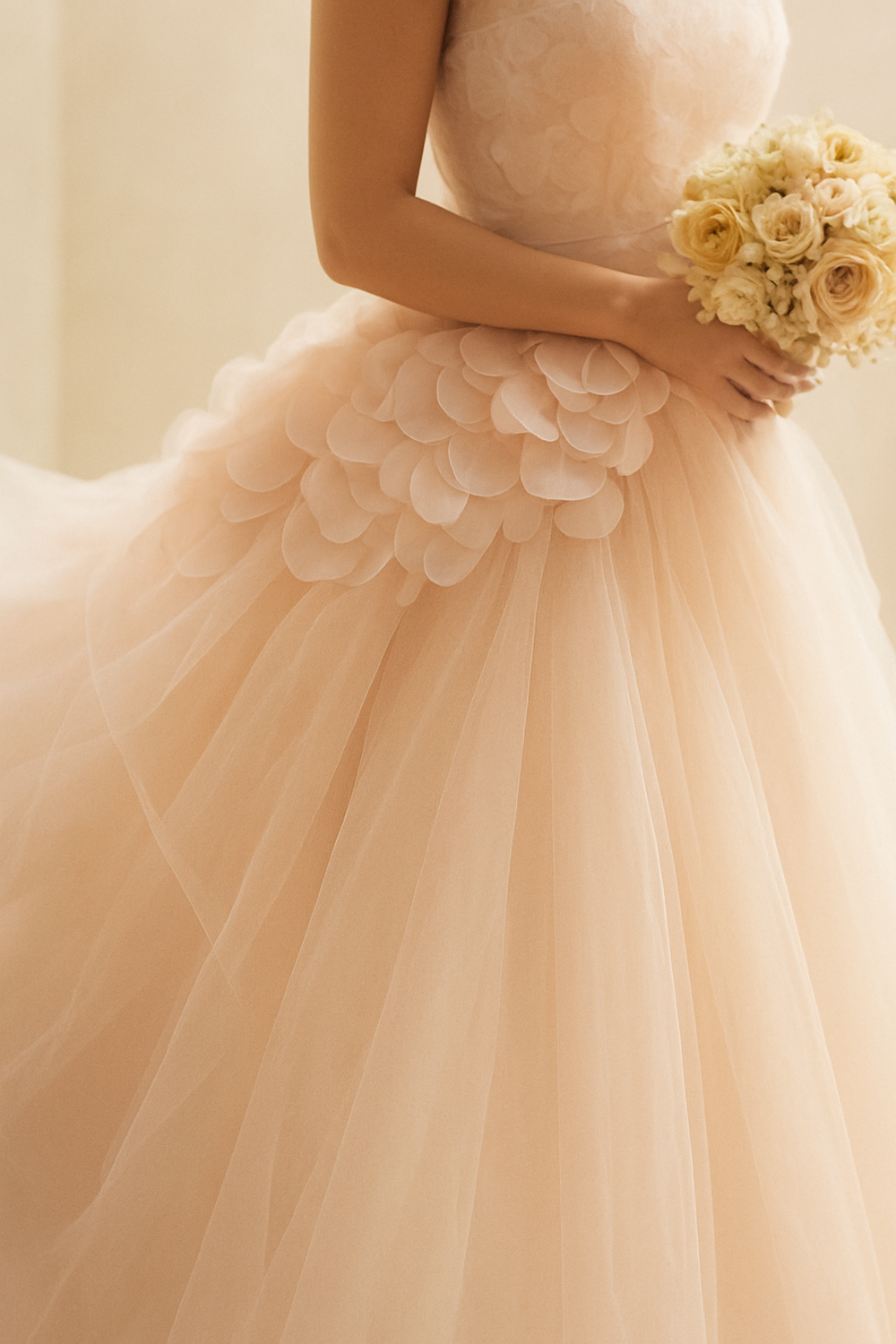A blush tulle wedding dress and a bouquet of cream roses