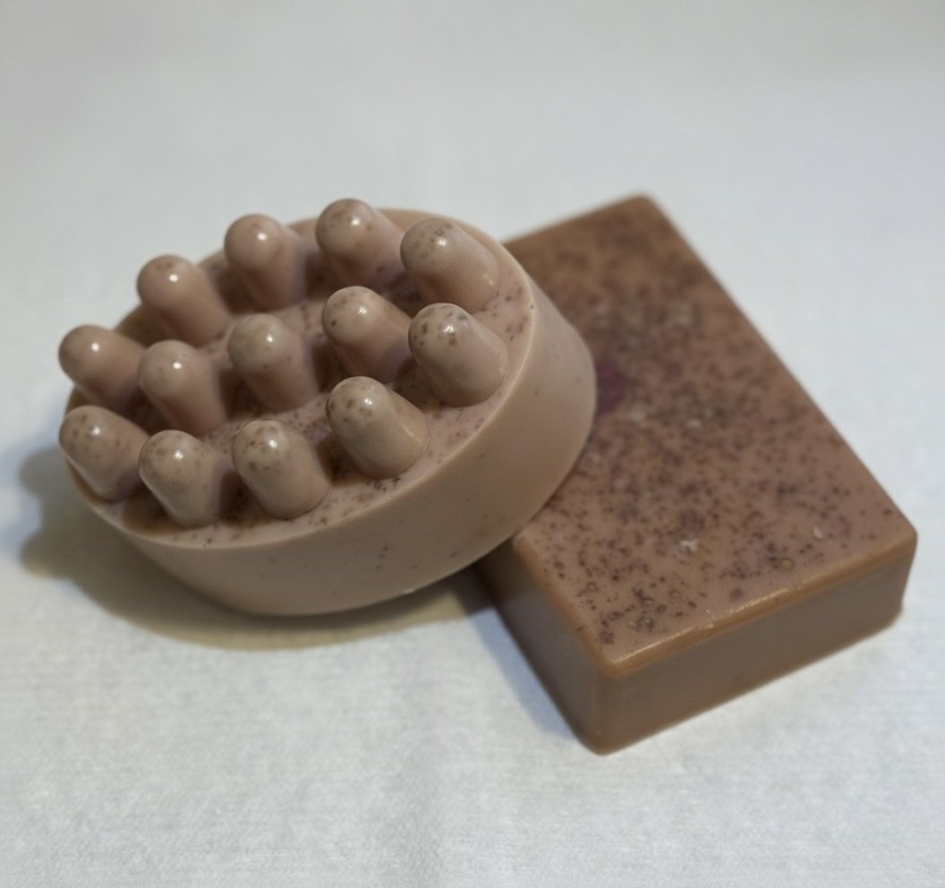 Two pieces of soap, one oval-shaped with multiple rounded protrusions on top, and one rectangular with a speckled pattern, both in shades of beige and brown.