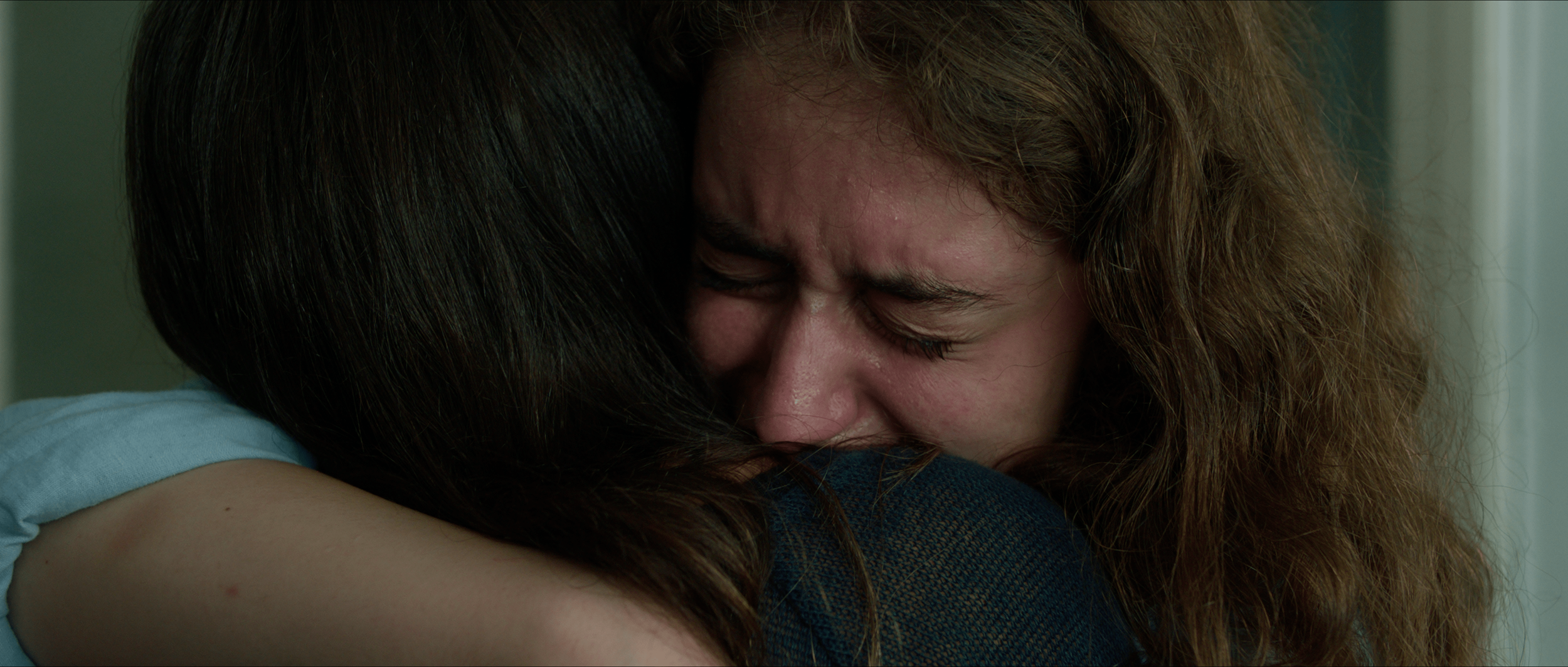 Two women hugging tightly, one crying with eyes closed and a distressed expression.