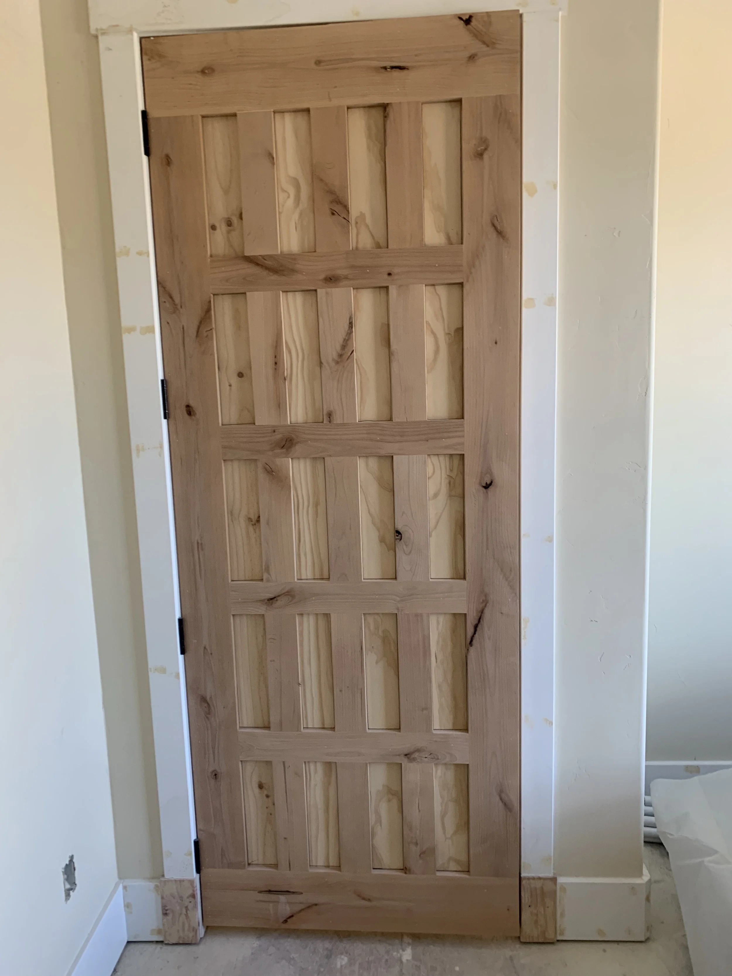 Unfinished wooden door with rectangular panels leaning against a wall in a room under renovation.