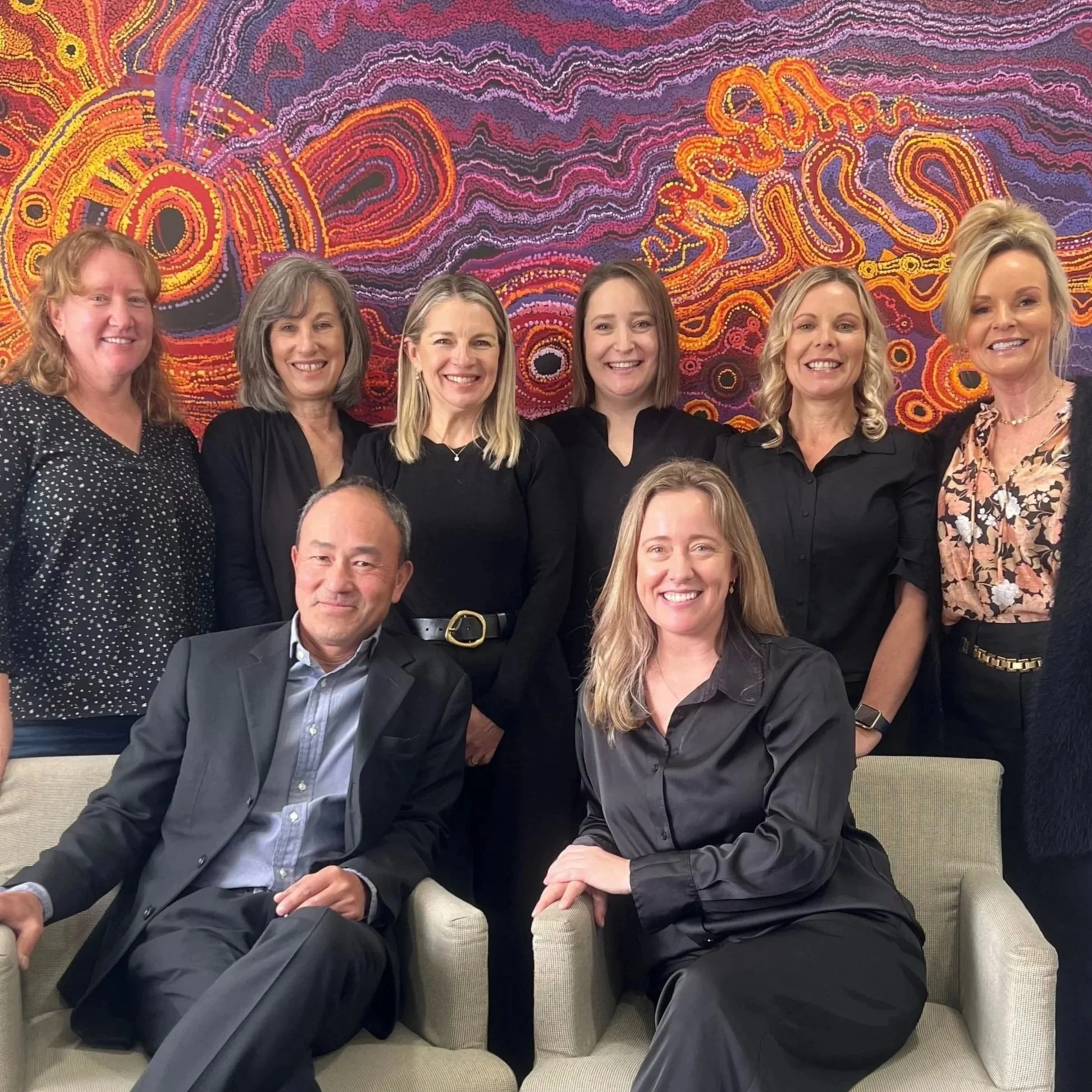 Group of people sitting and standing in front of colorful abstract wall art, smiling at the camera