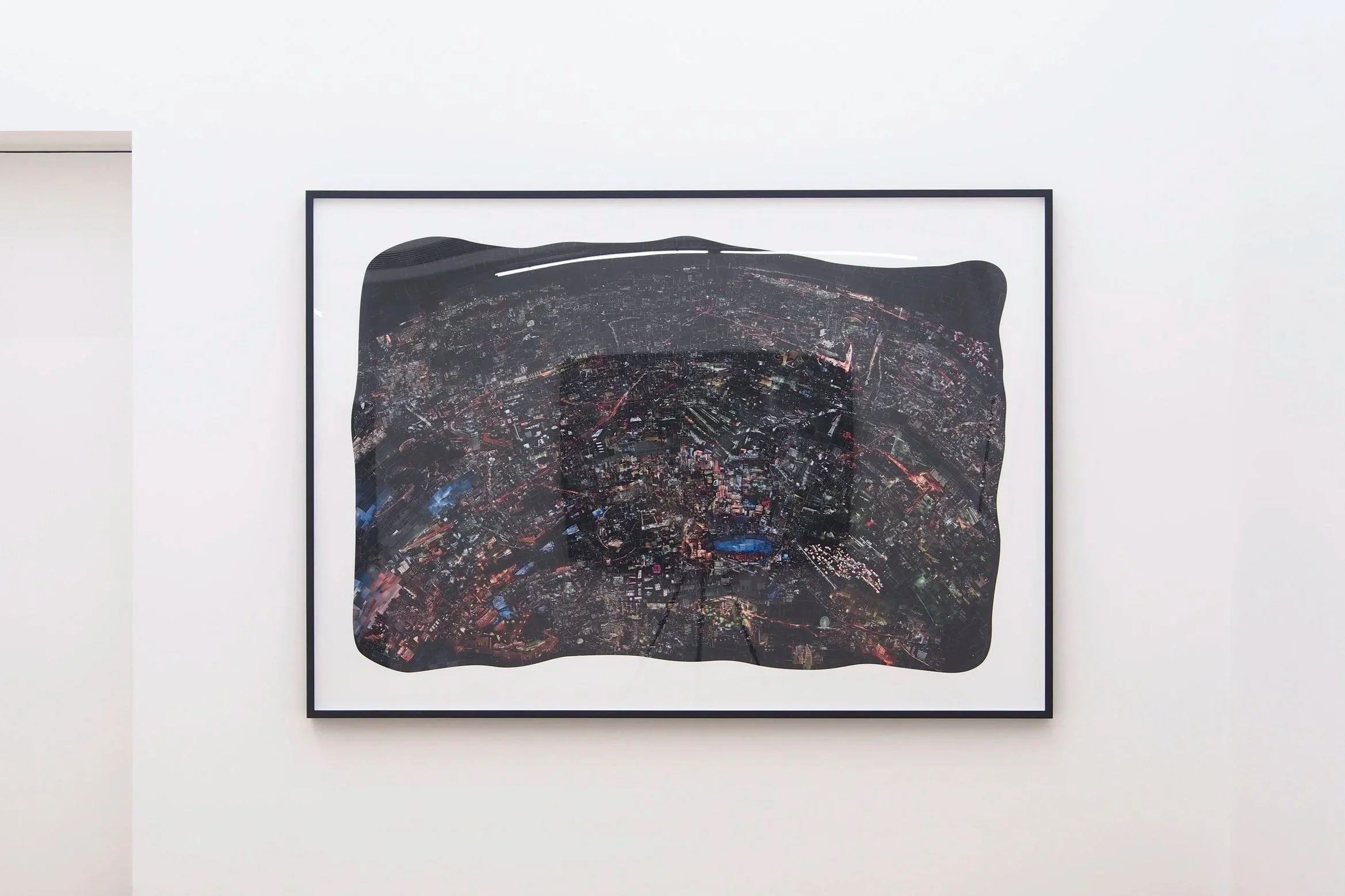 都市の夜景を映したアート作品が白い壁に掛けられている。」}