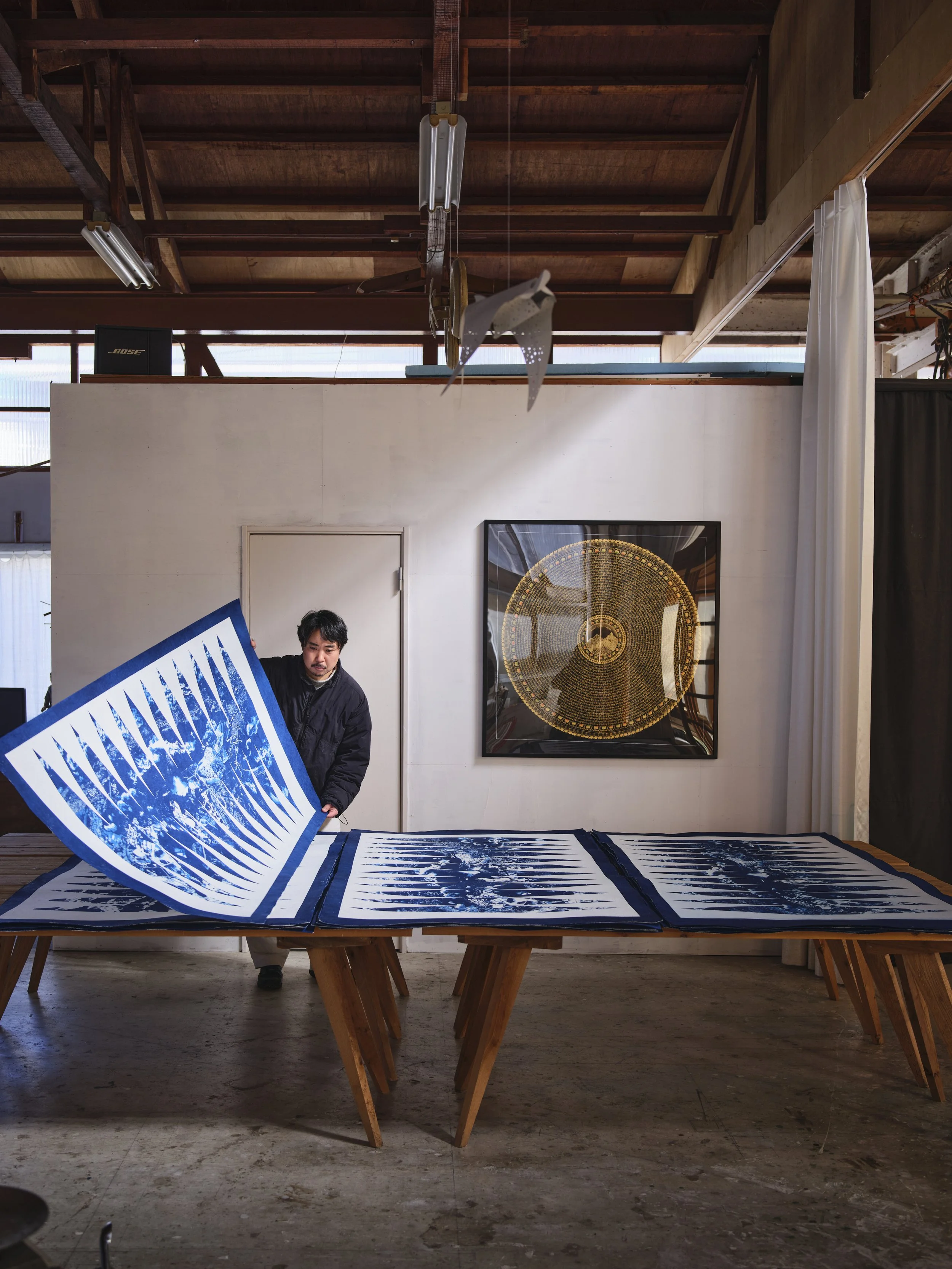 男性が青と白の絵を広げている工房の部屋。壁には金の時計のアートが掛かっている。