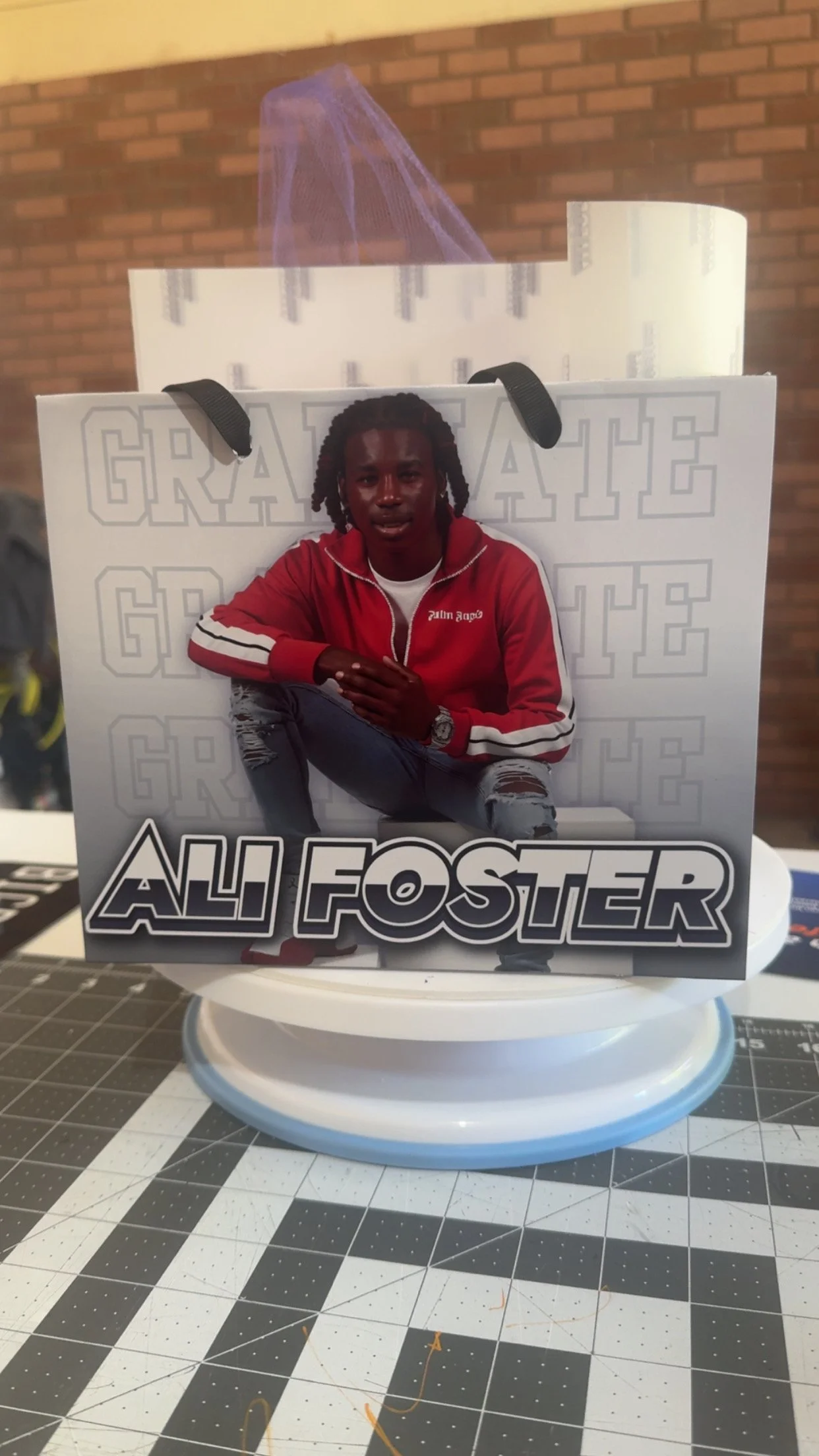A cardboard standee featuring a young man in a red jacket with black and white stripes, ripped jeans, and dreadlocks, with the name 'Ali Foster' prominently displayed at the bottom.