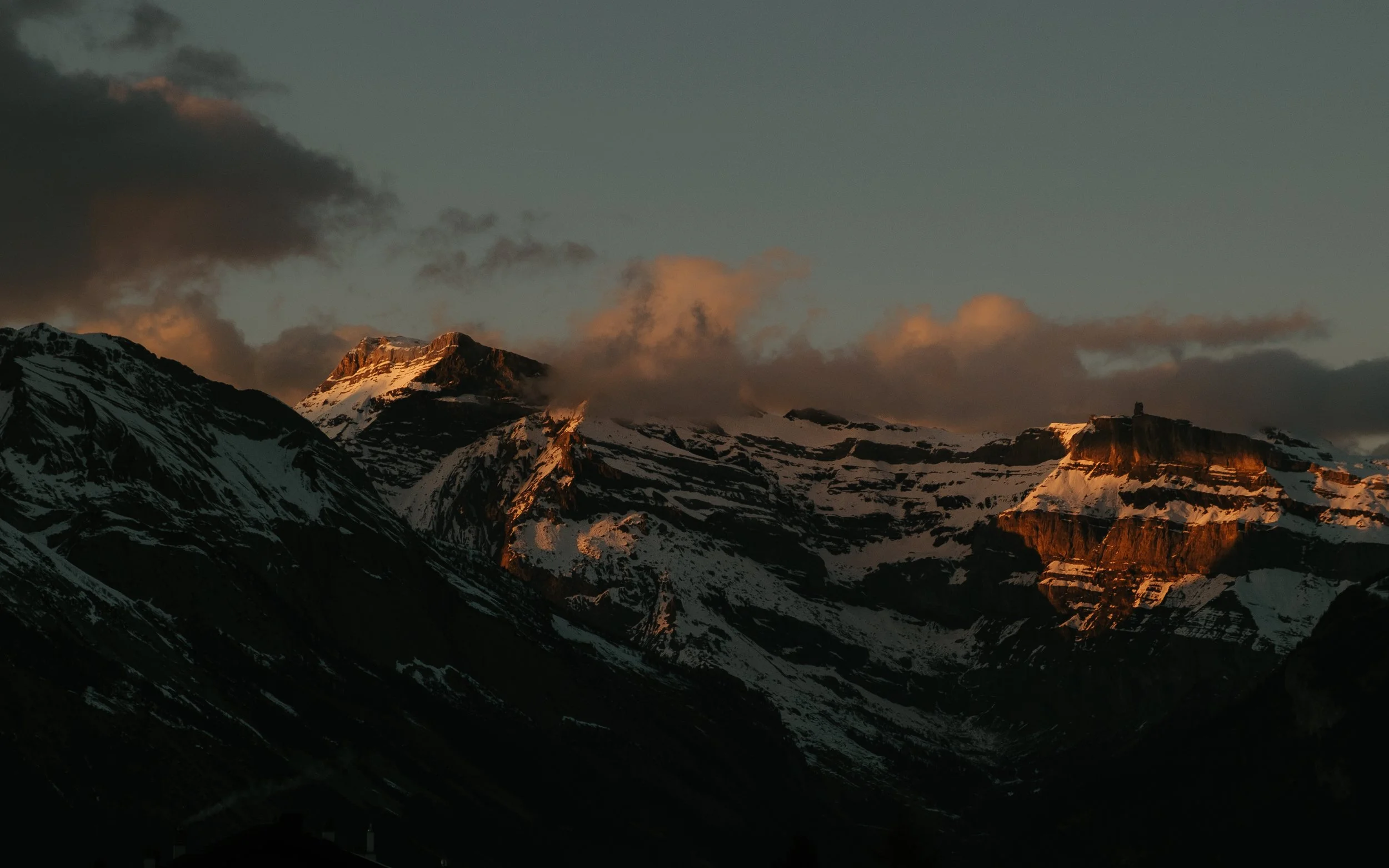 Sunset illuminating snow-capped mountains with clouds in the sky.
