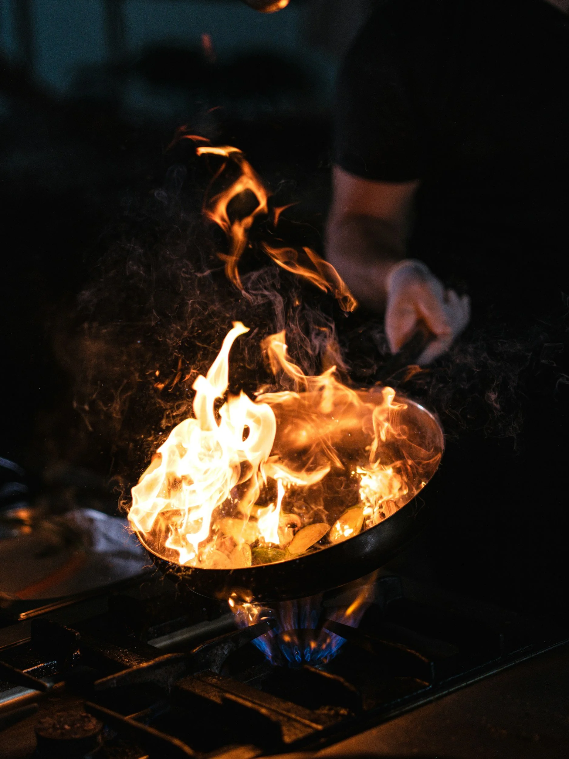 A person cooking on a stove with flames coming from a frying pan.