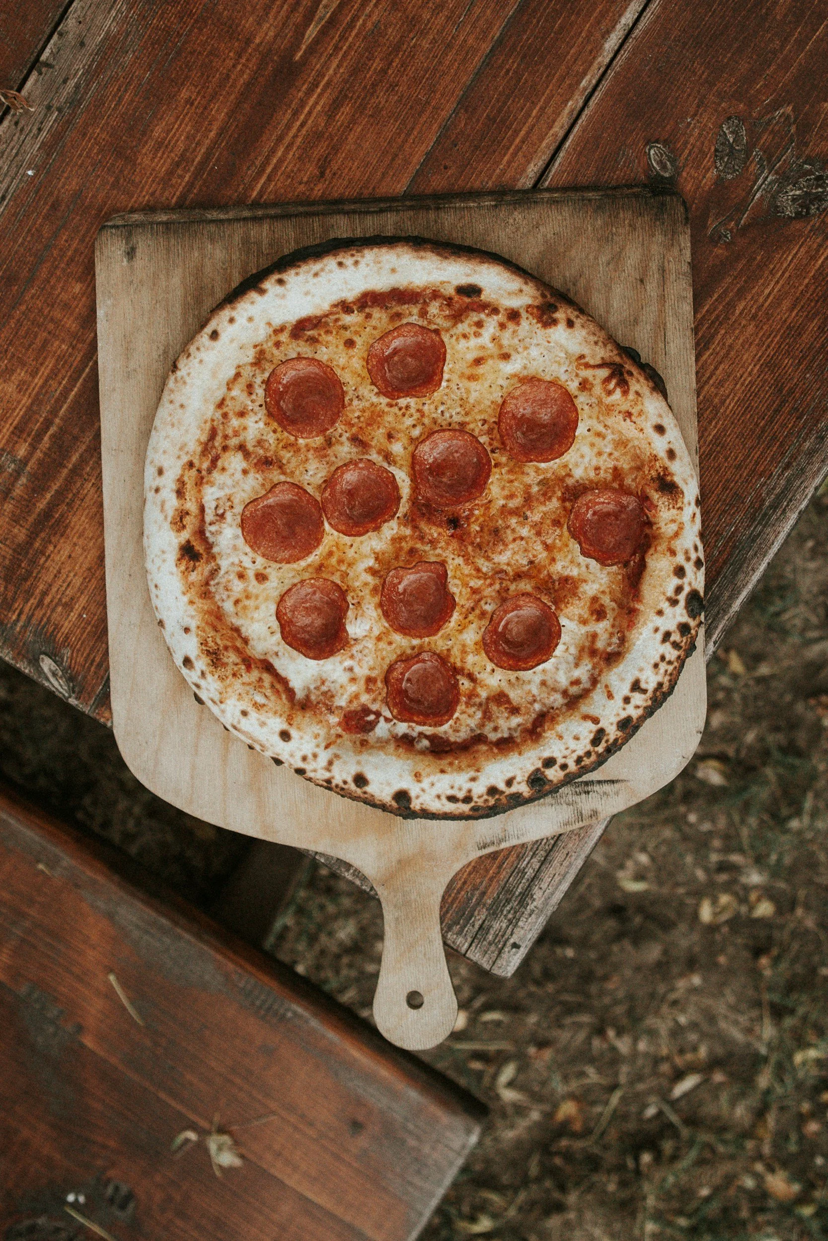 Pepperoni pizza on a wooden serving board placed on a rustic wooden table.