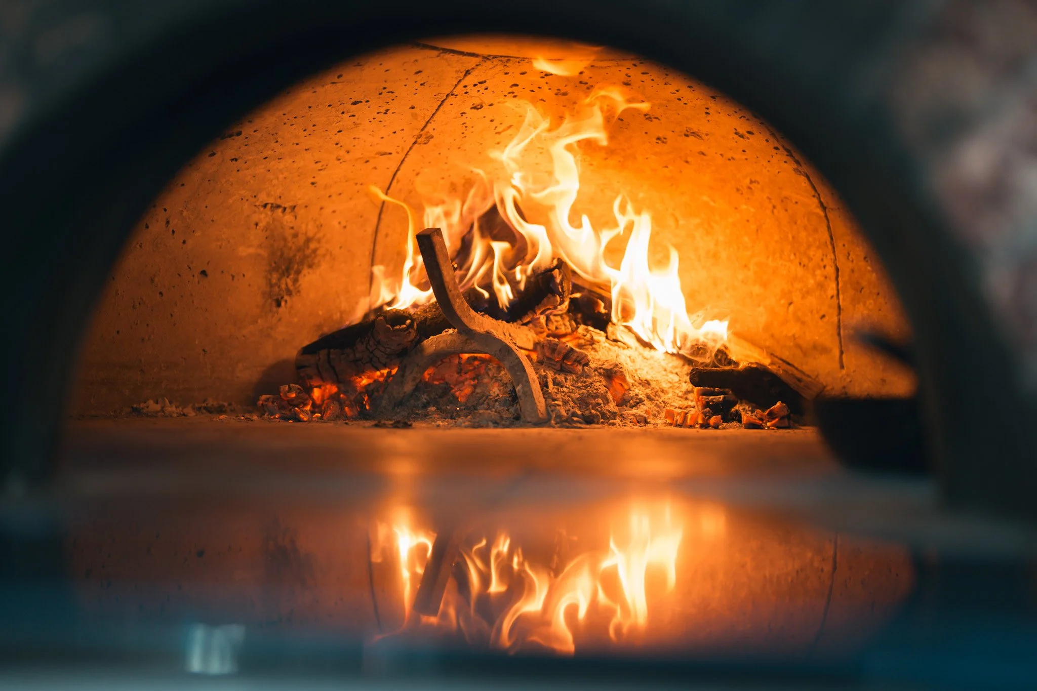Fire burning inside a pizza oven with a curved metal opening, showing flames and logs.