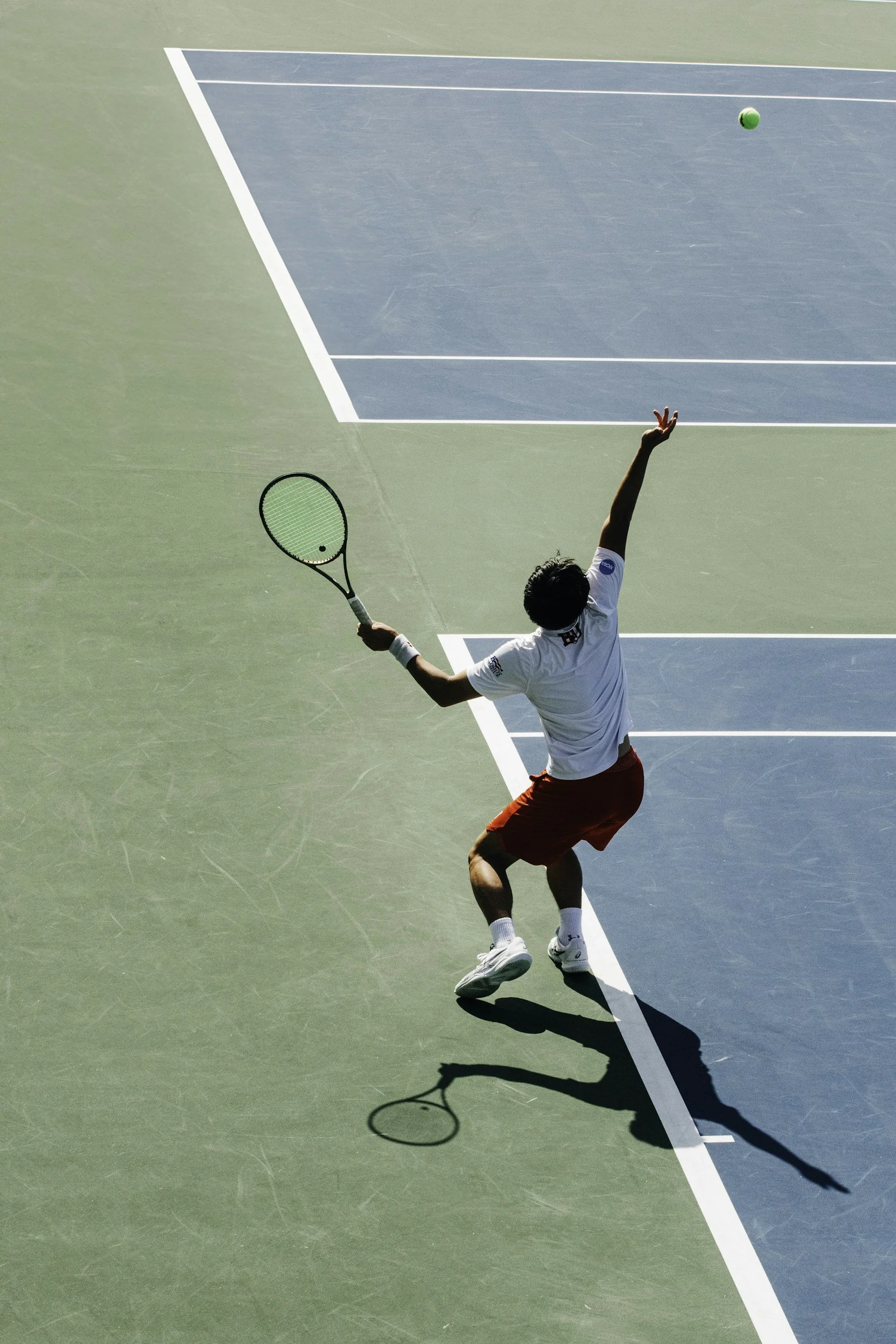 A man playing tennis on a court, hitting a green tennis ball with a racket.