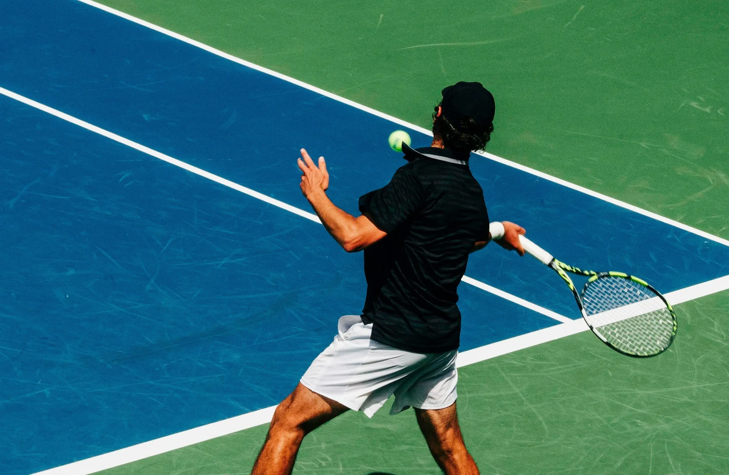 A man playing tennis on a green and blue court, preparing to hit the tennis ball with a tennis racket.