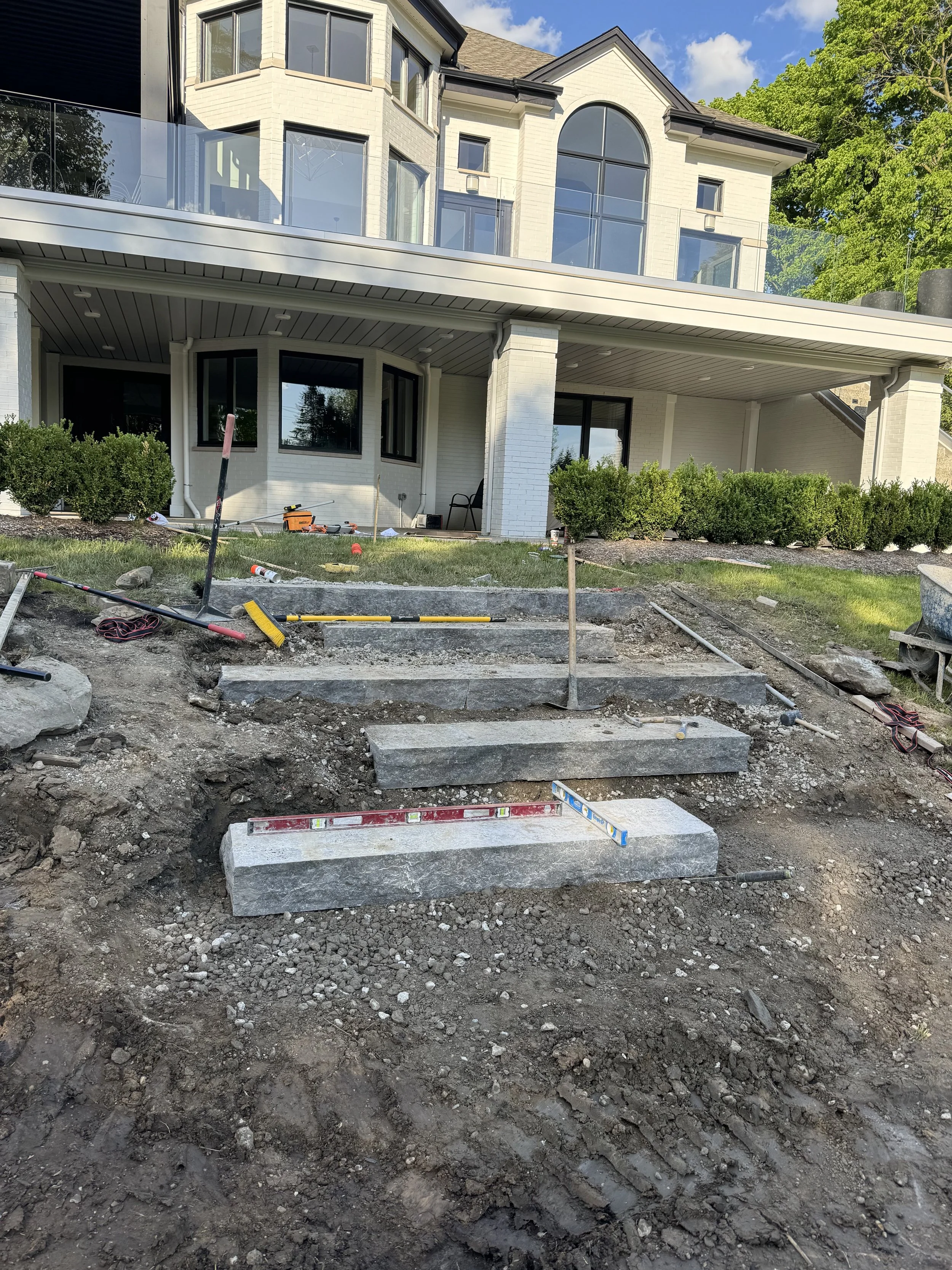 Construction site in front of a modern house with stairs being built, surrounded by tools and dirt.