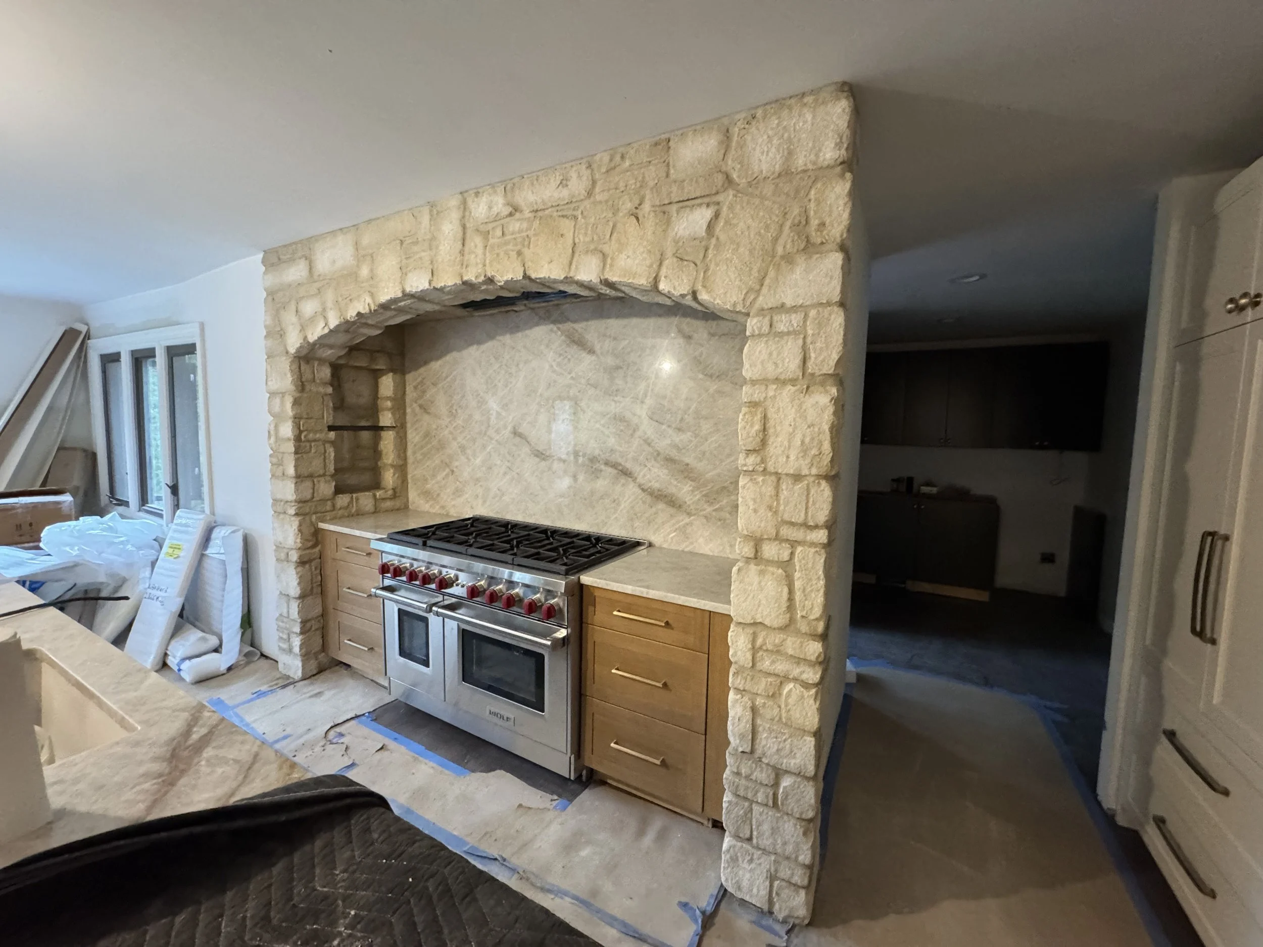 Kitchen with a stone archway framing a stove, with wooden cabinets and marble or stone backsplash.
