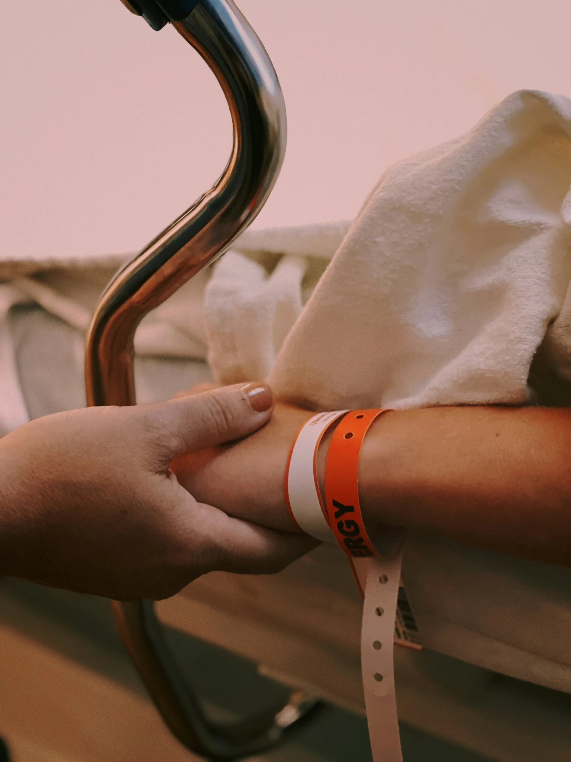 hand holding another hand of a person on a gurney, orange arm band