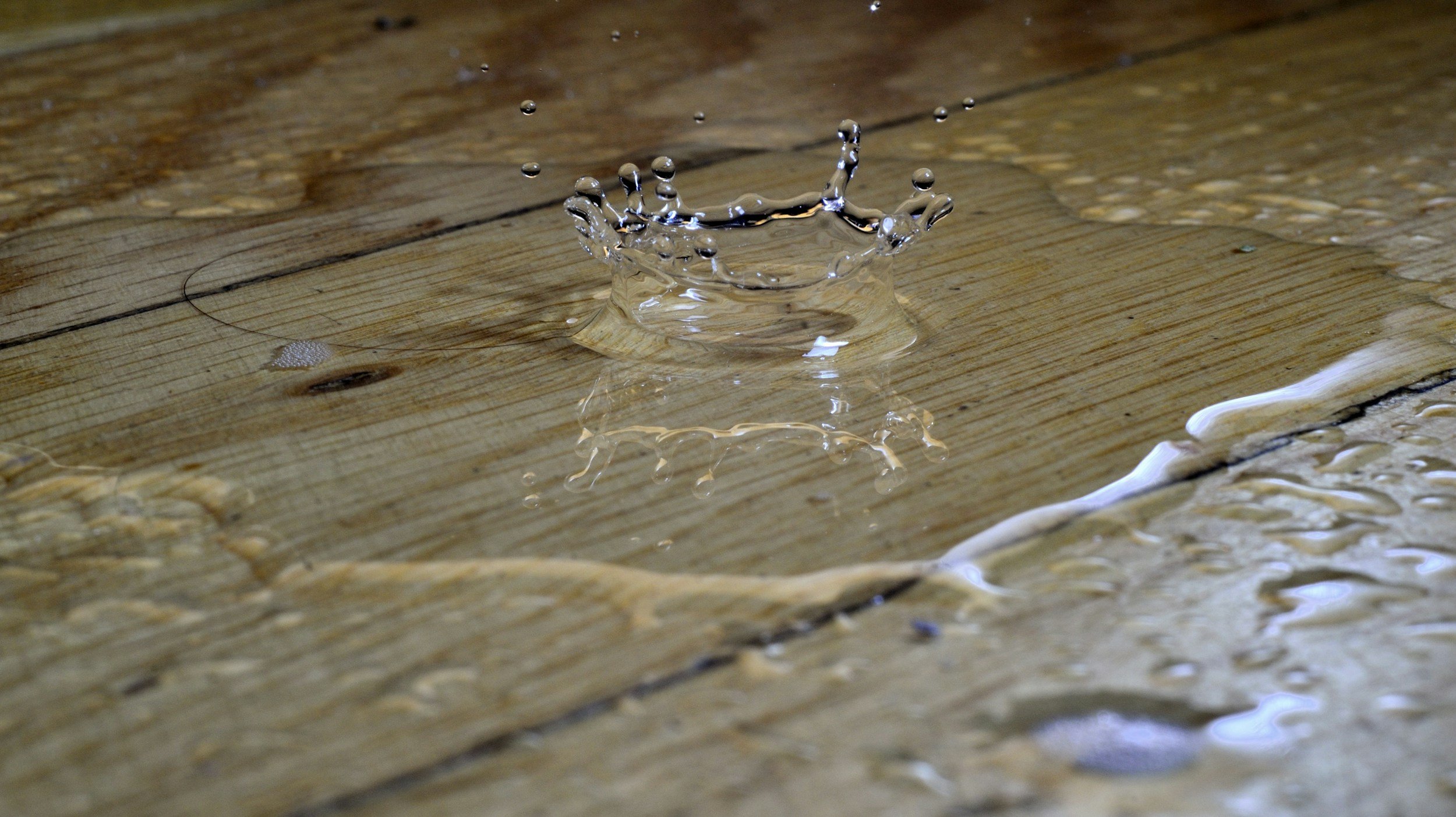 A water droplet hitting a wooden surface, creating a splash and ripples.