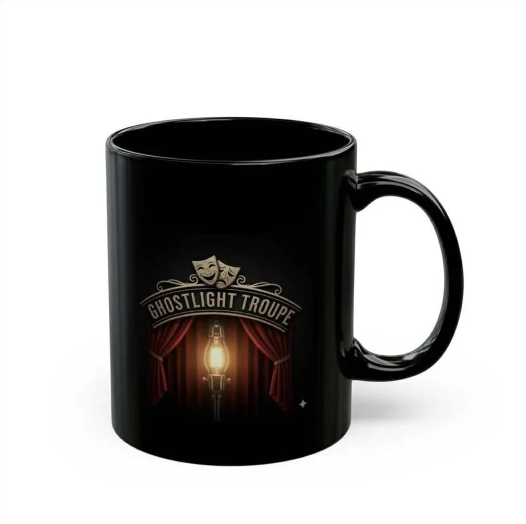 Black ceramic mug featuring the logo of Ghostlight Troupe with theatrical masks, a stage curtain, and a lantern.