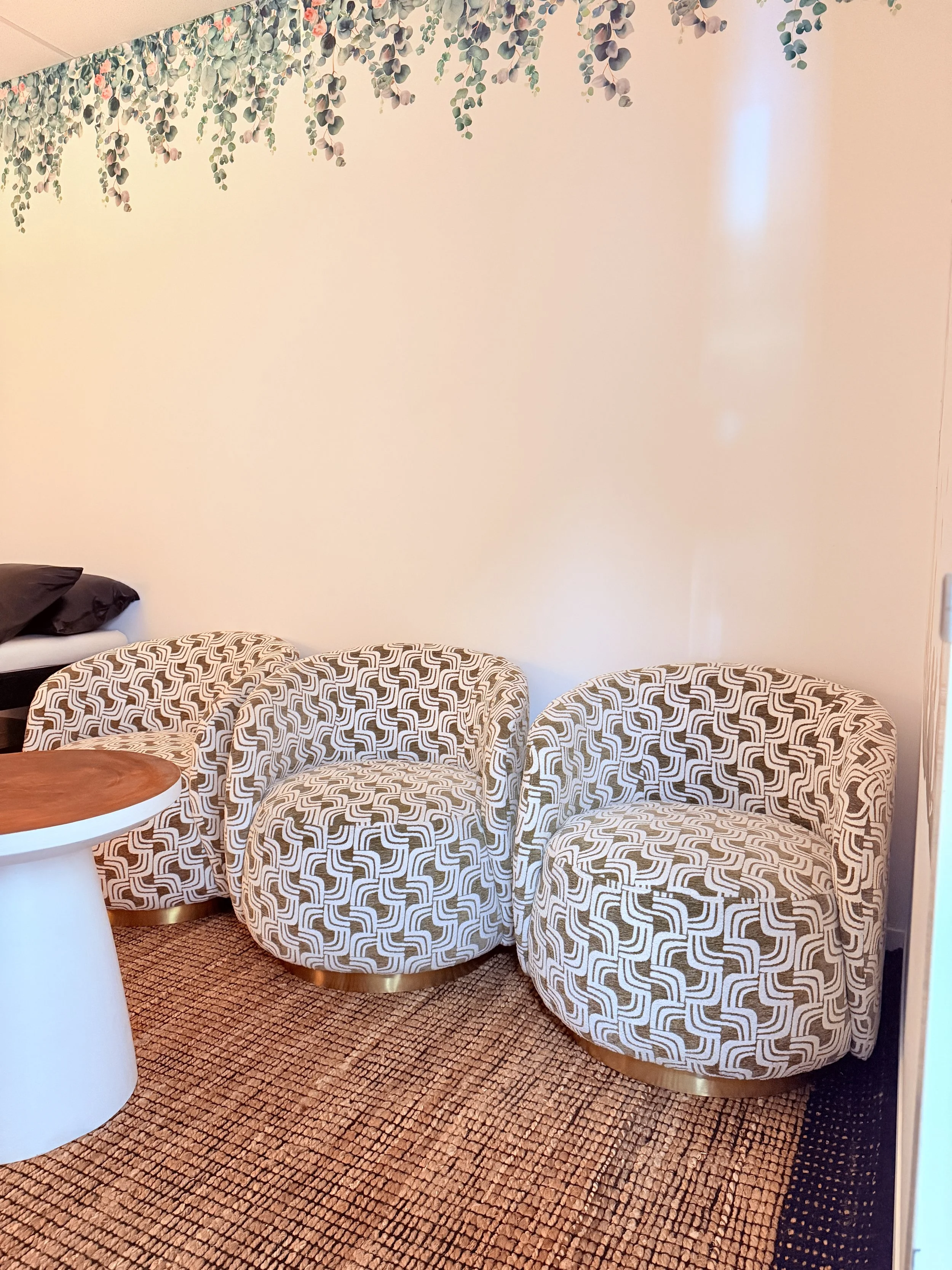 Comfortable family seating area at Cedar 4D Ultrasound featuring patterned armchairs, a round wooden table, soft furnishings, nature-inspired wall décor, and a warm, welcoming studio environment.