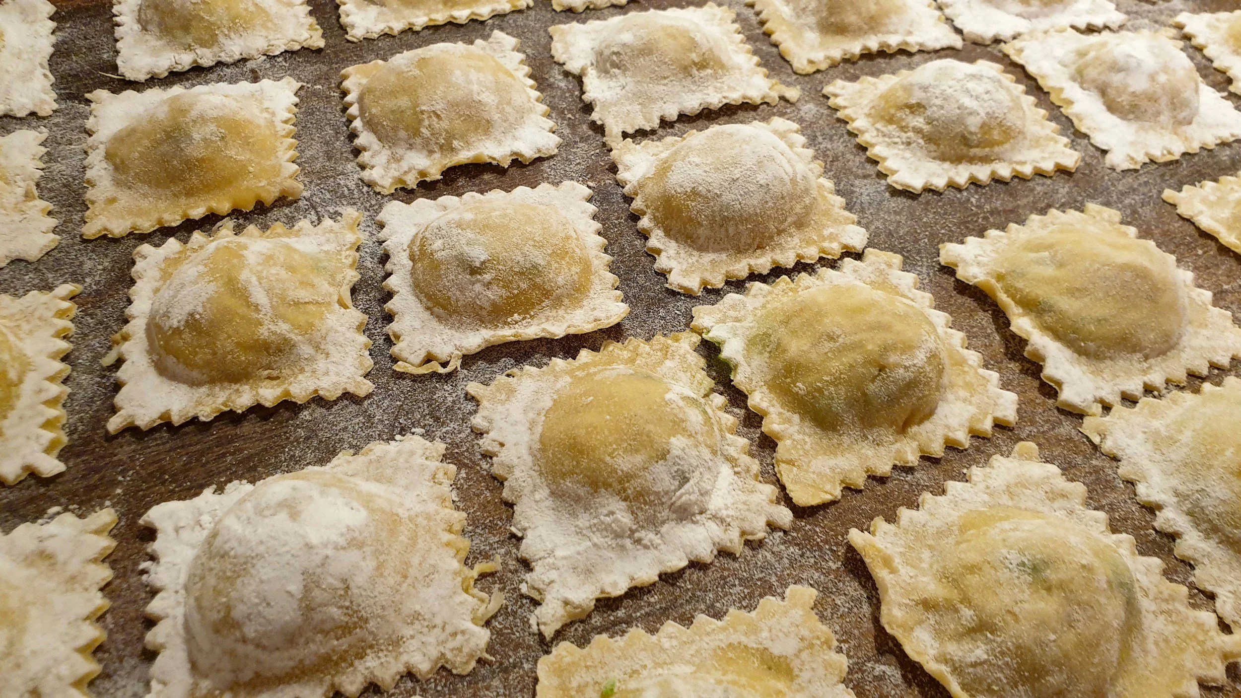 Uncooked ravioli pasta with filling dusted with flour, arranged on a baking sheet.