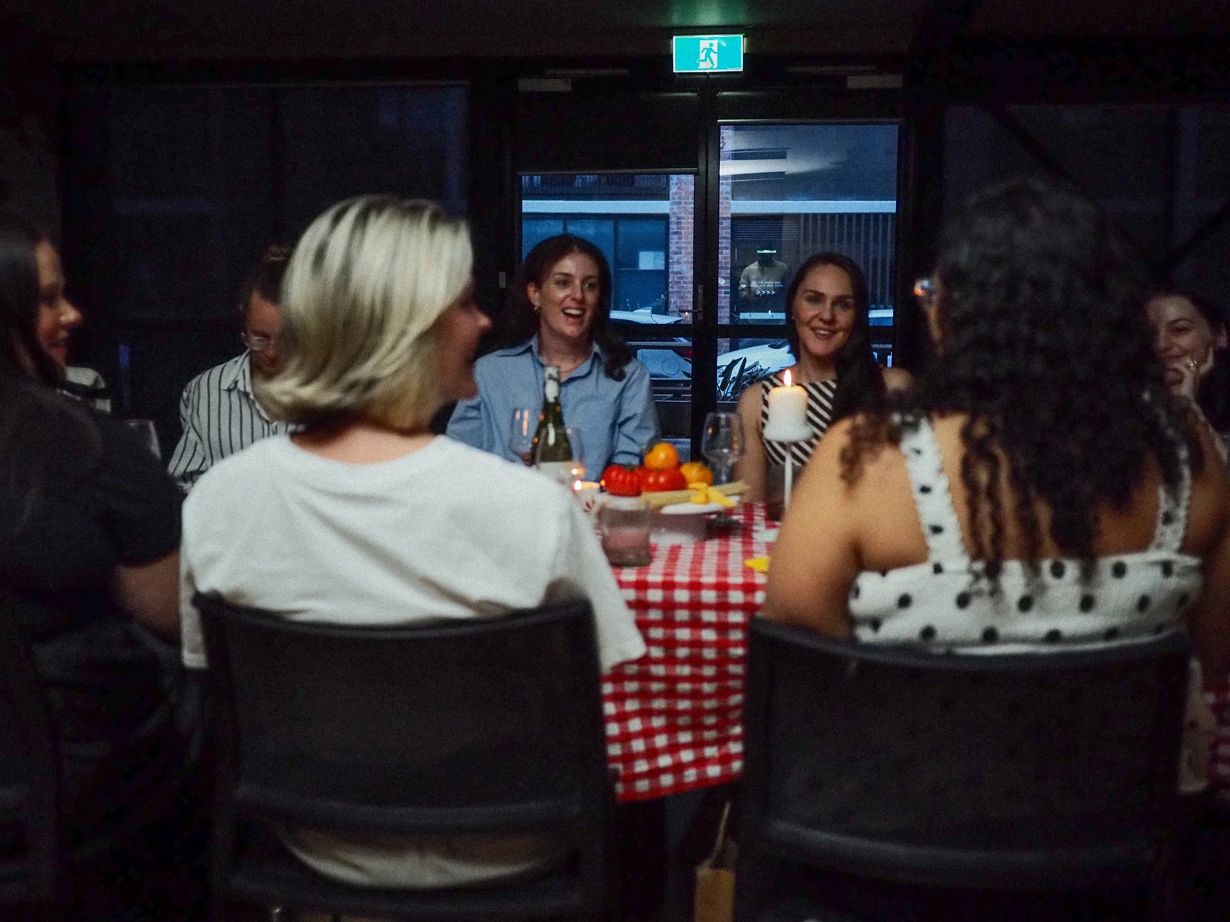 Group of women sitting around a table having a celebration with candles and food, in a dimly lit room.