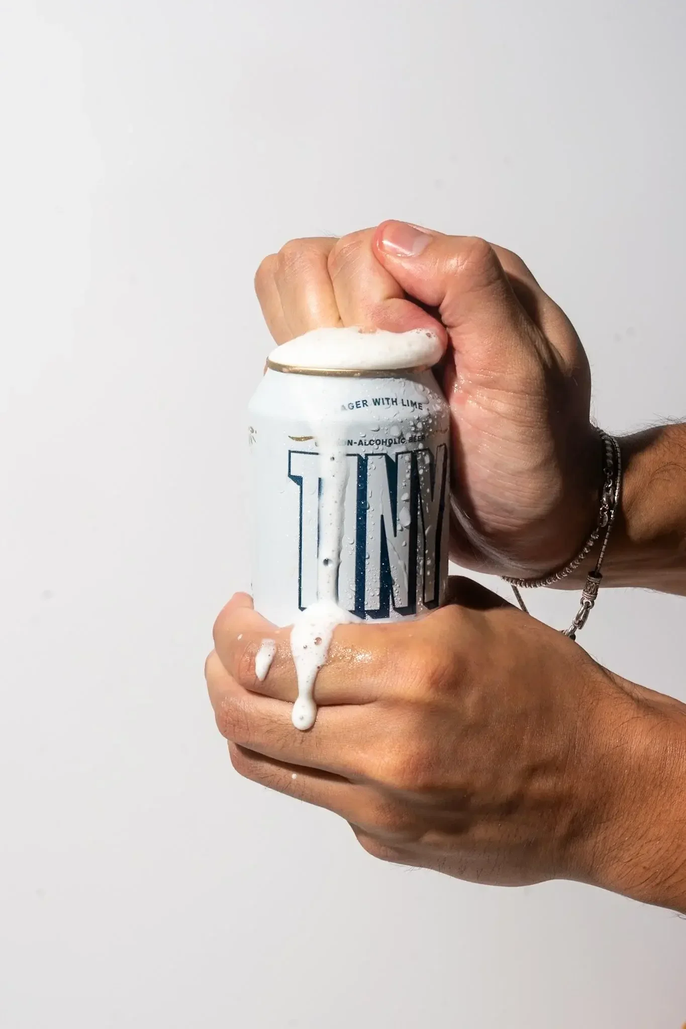 A person holding a can of alcoholic sparkling water with foam and liquid overflowing from the top.