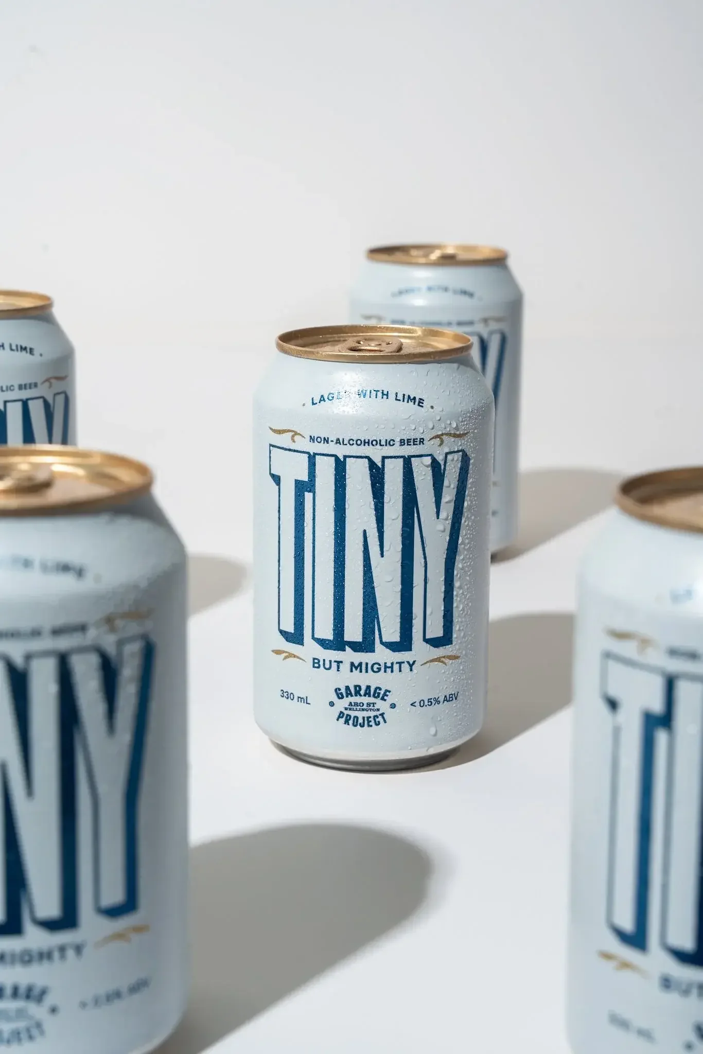 Cans of non-alcoholic beer labeled 'TINY but mighty' with condensation droplets on the surface, arranged on a white surface.