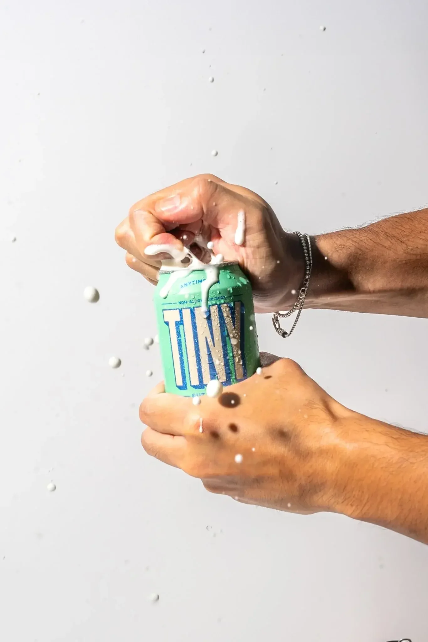Two hands are opening a can of whipped cream, with foam spraying out onto a white surface.