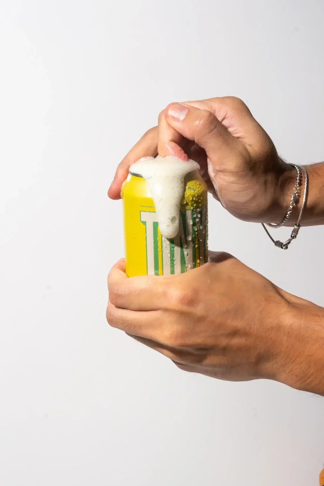 Person opening a yellow soda can with foam overflowing from the top.