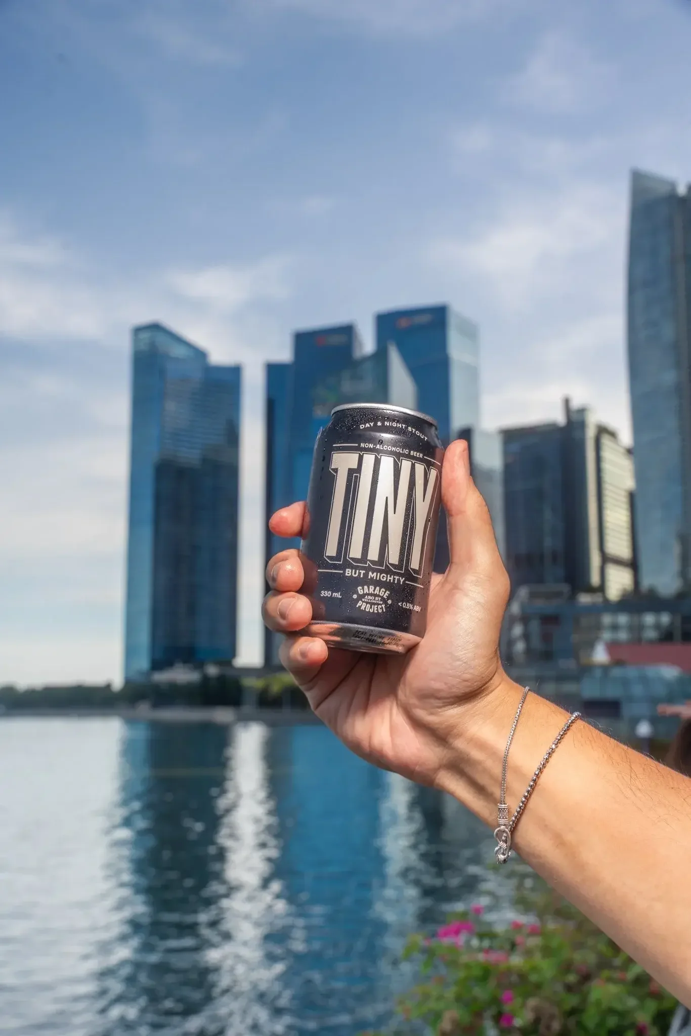 A person holding a can of non-alcoholic beer with a city skyline and river in the background.