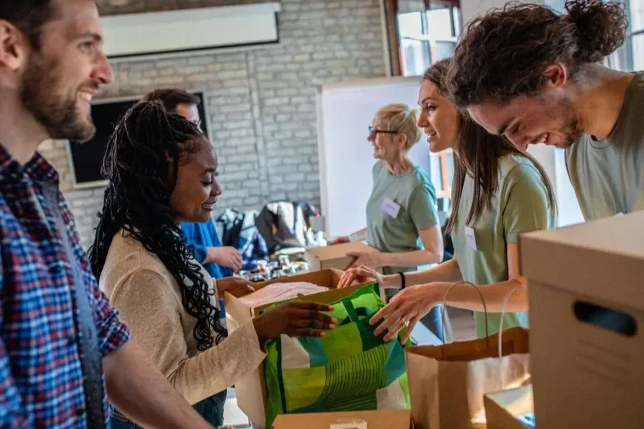 People handing out and receiving items at a charity or donation event in a room with large windows and brick walls.