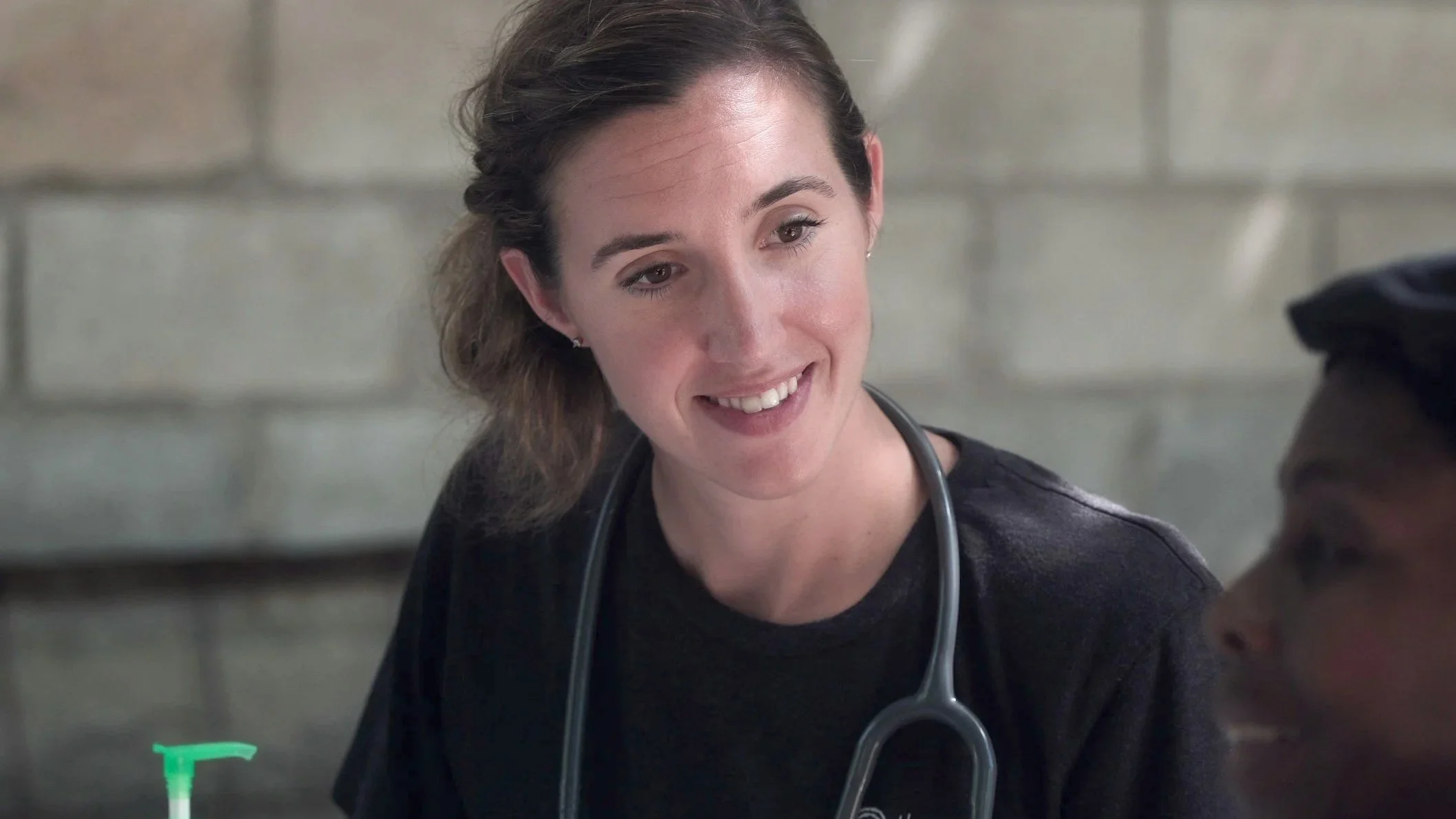 A female doctor with a stethoscope talking to a patient in a healthcare setting.