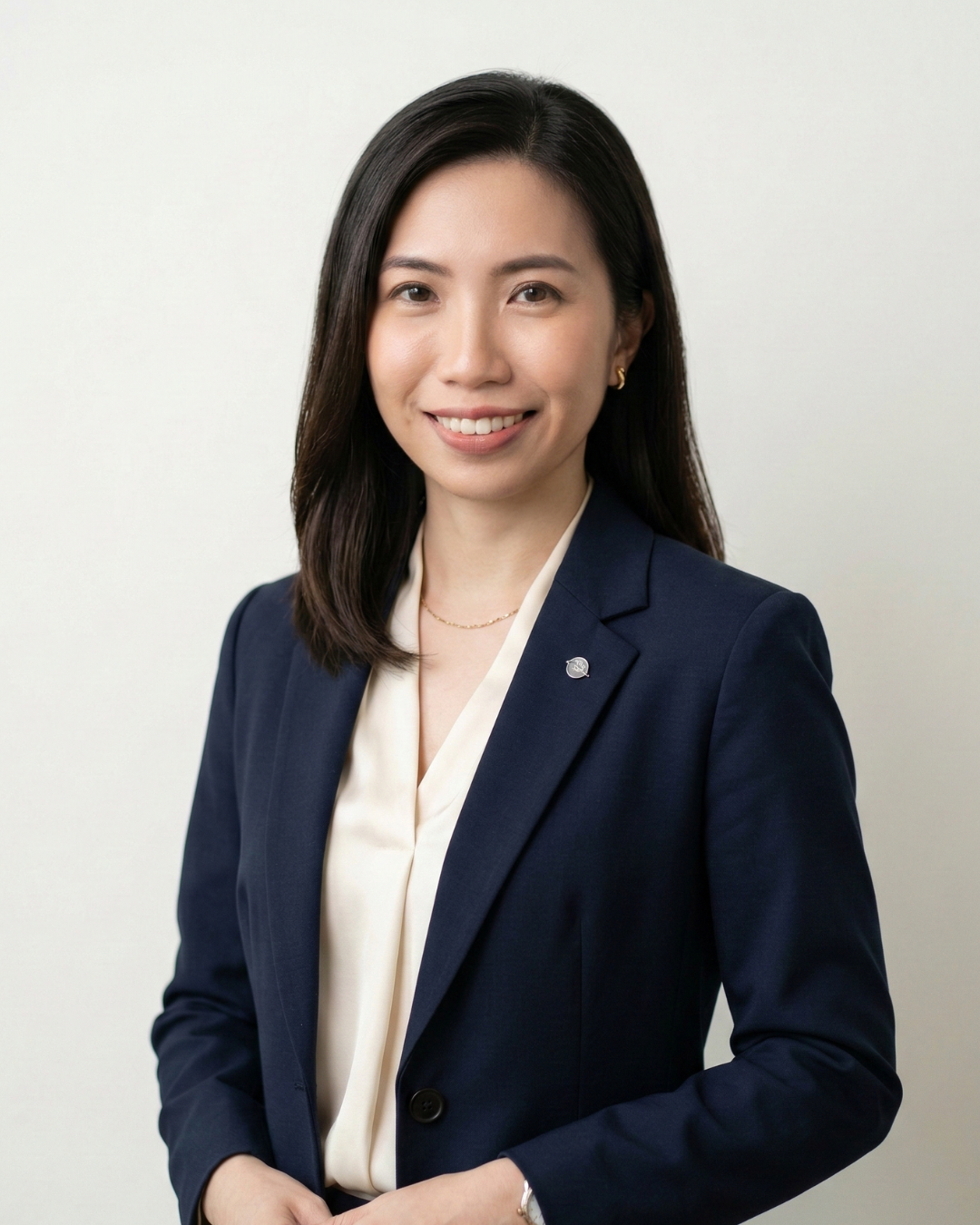 Professional woman with shoulder-length black hair in navy blazer and cream blouse, smiling against a plain light background.