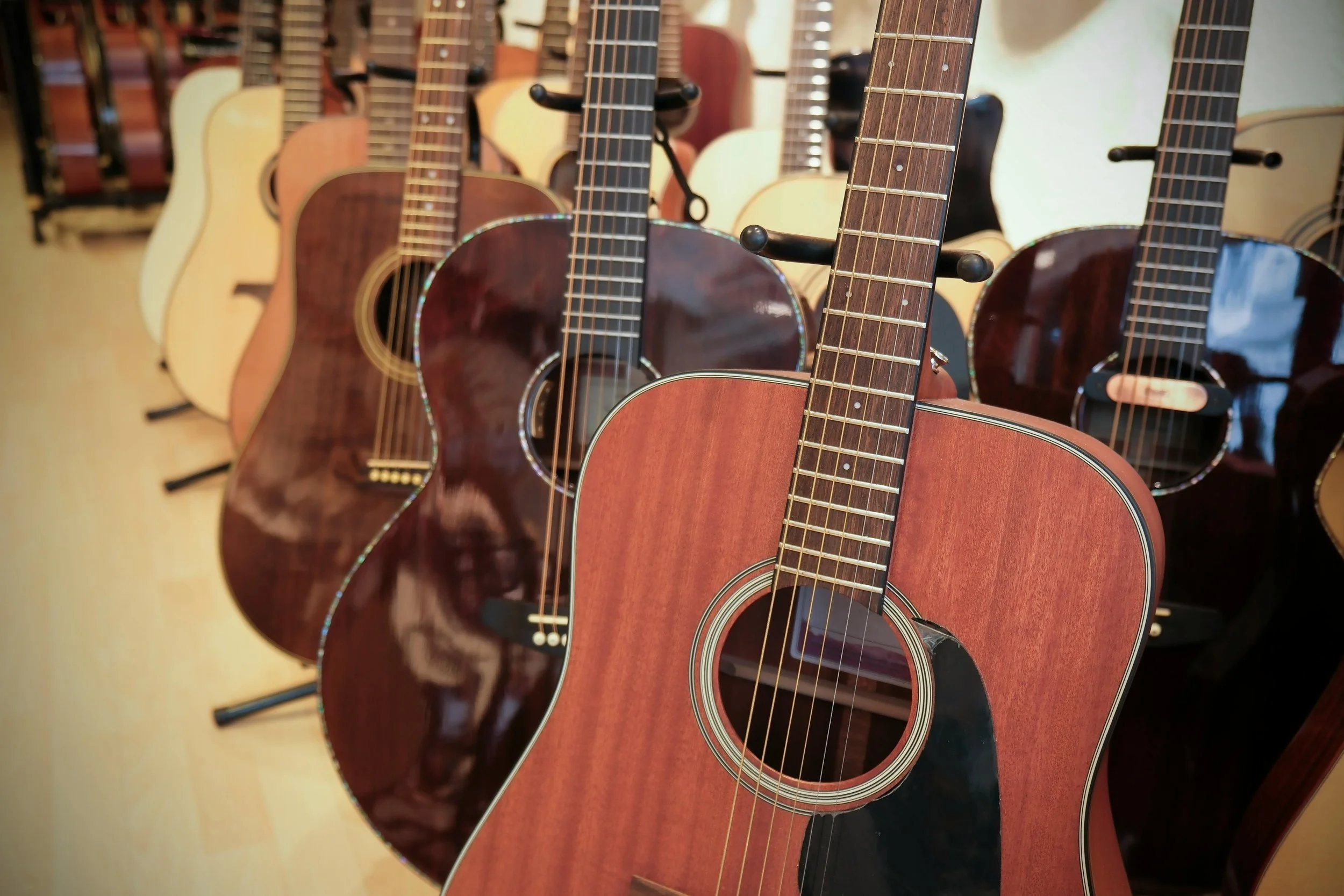 Several acoustic guitars hanging on a wall, with the focus on a reddish-brown guitar in the foreground.
