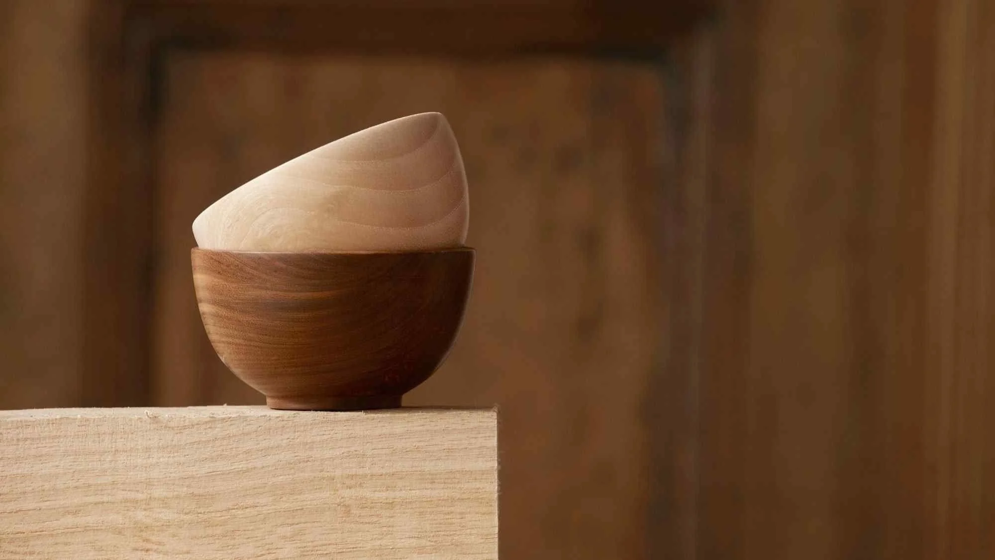 Stacked wooden bowls, light and dark wood, on a wooden surface with a blurred wooden background.