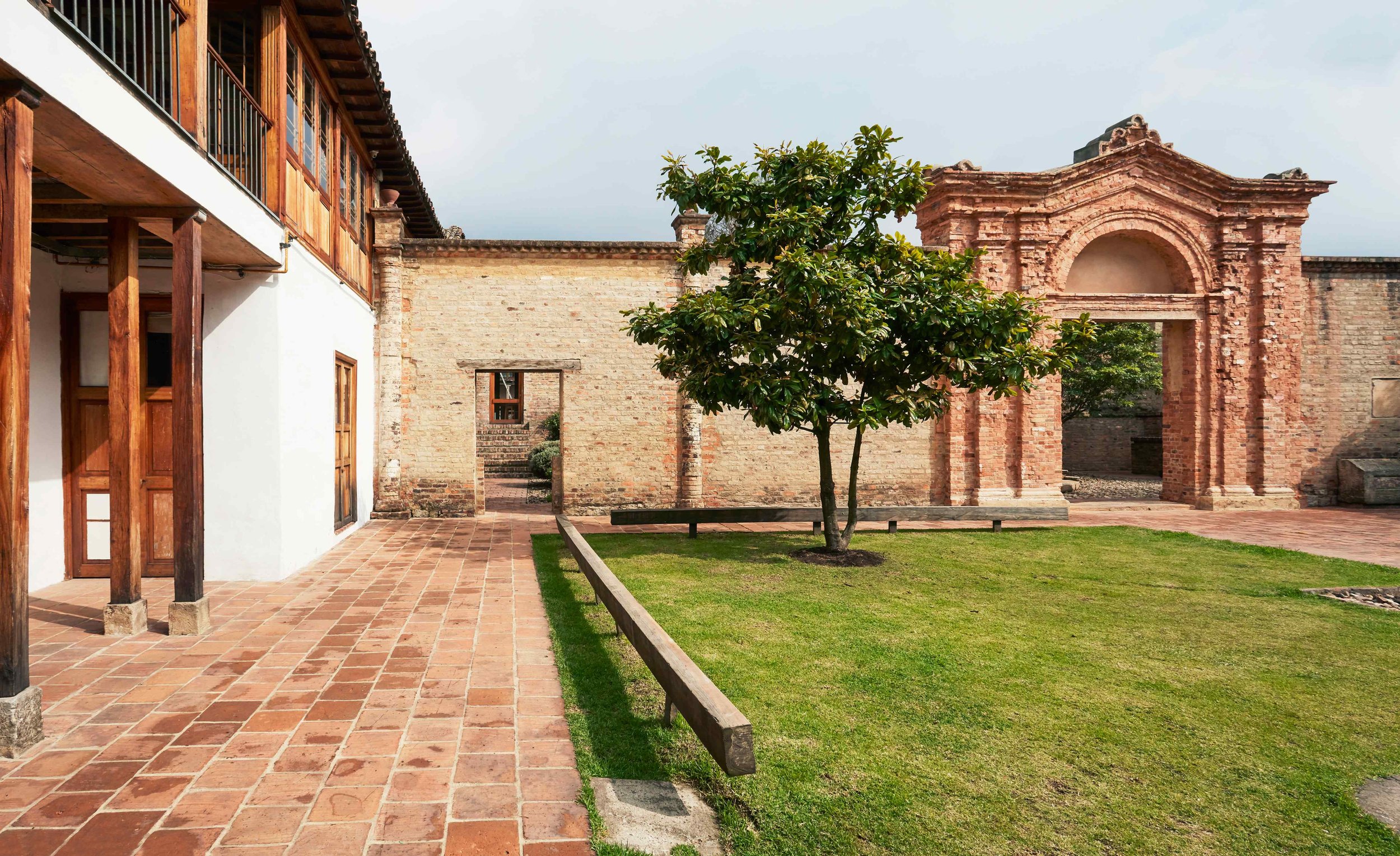Courtyard with brick pathway, green grass, a small tree, and historic brick archway.