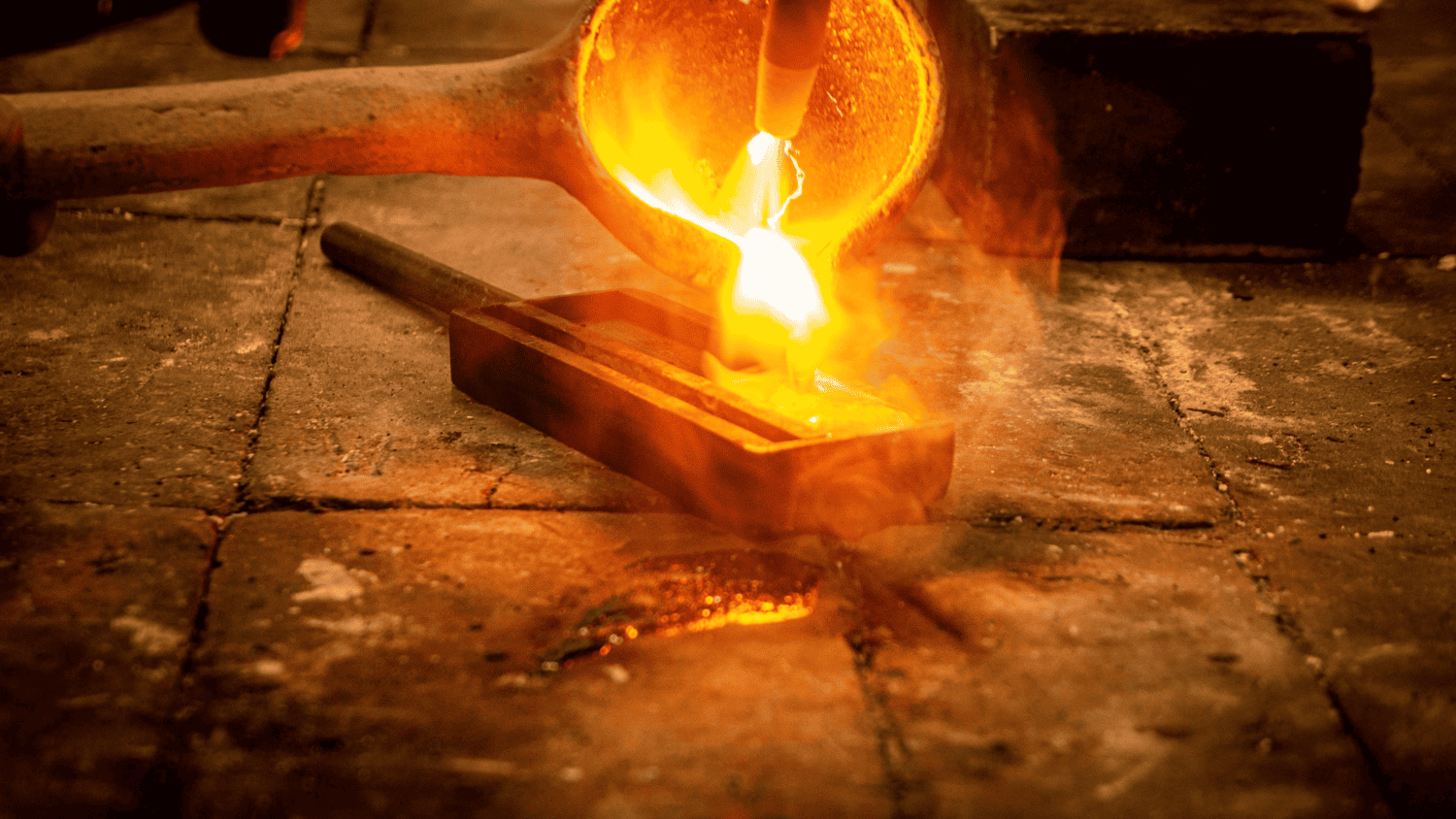Person using a mallet to forge a metal pipe with a hammer, wearing a blue jacket and pants.