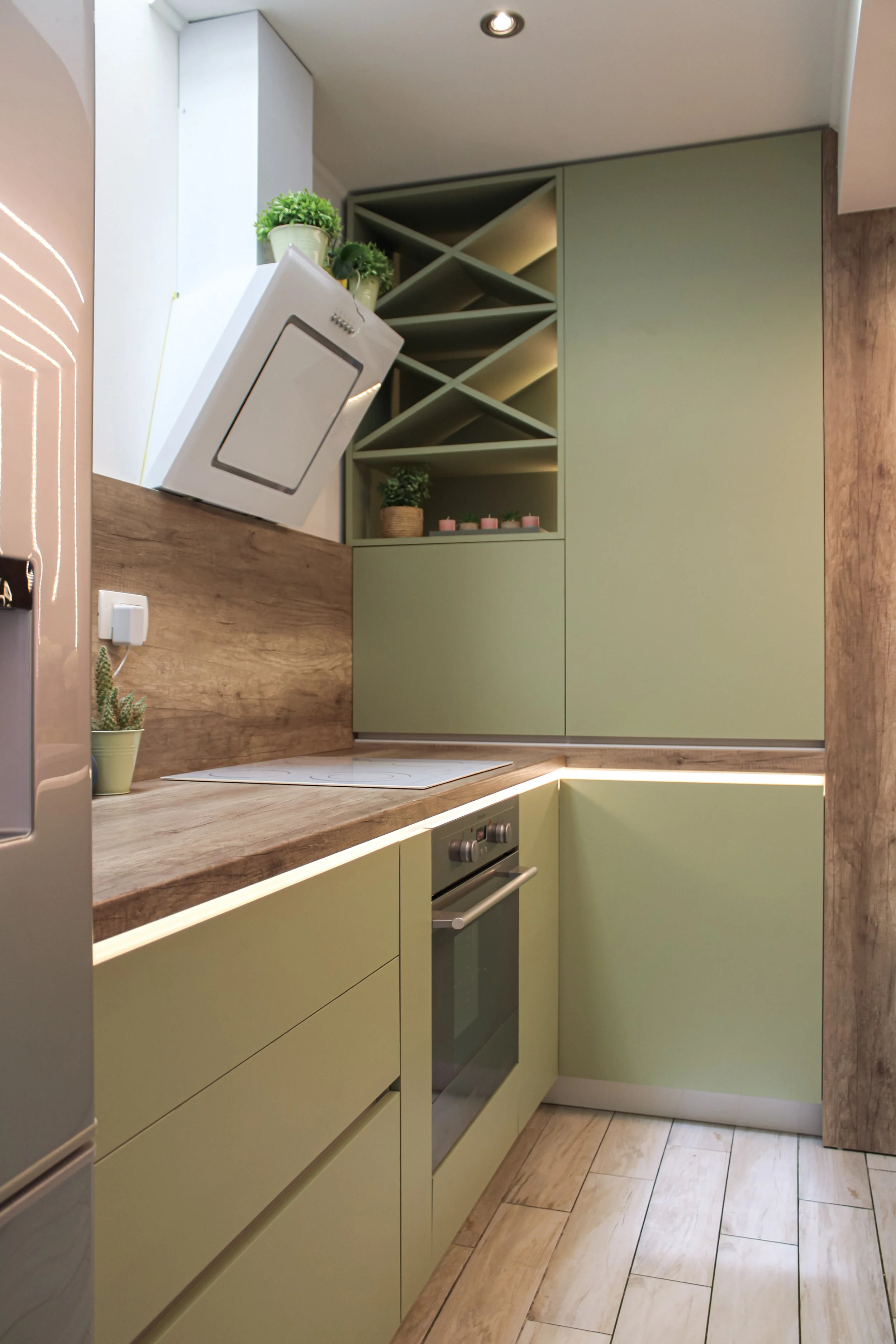 Small modern kitchen with matte green cabinets, built-in oven, wood accents and open wine rack, custom design by Bespoke Interijeri.